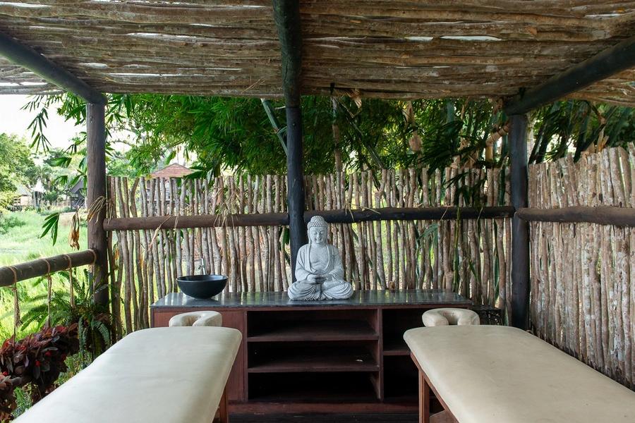 Two massage beds in an open-air pavilion with reed walls and a Buddha statue