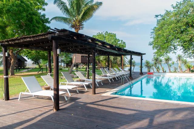 Swimming pool with sun loungers under a wooden pergola, palm trees and the lagoon beyond