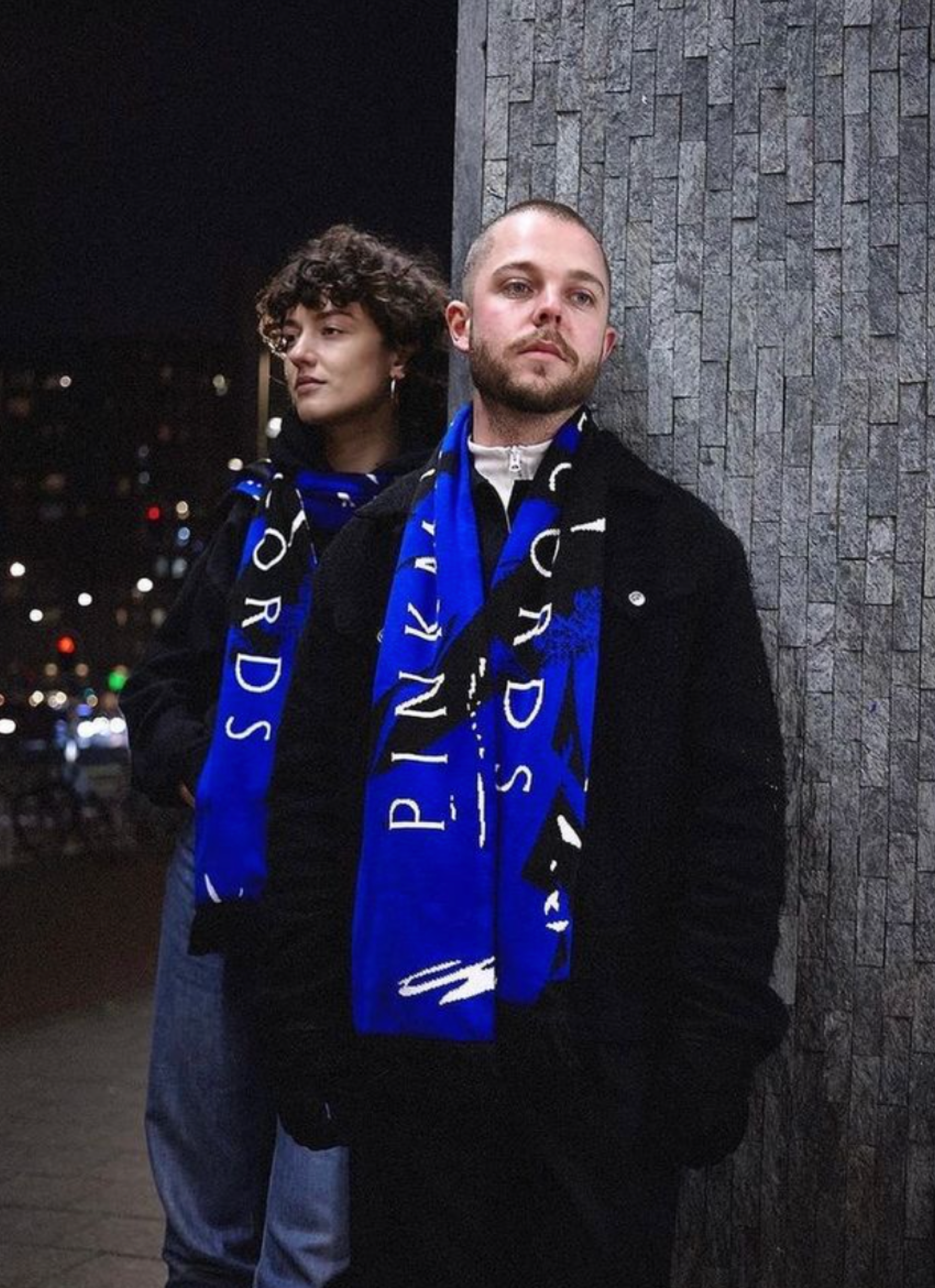 Two people in blue Pinkman Records scarves at night