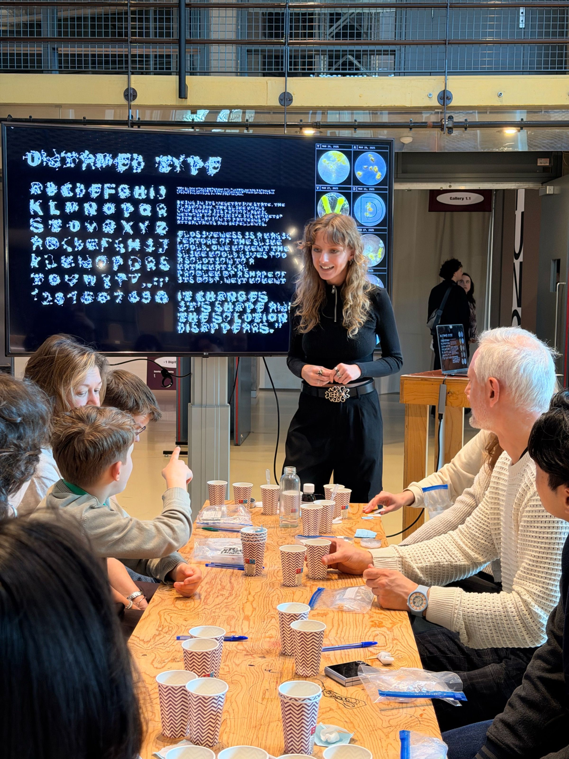 Workshop leader standing before a screen showing an experimental typeface, participants at a long table