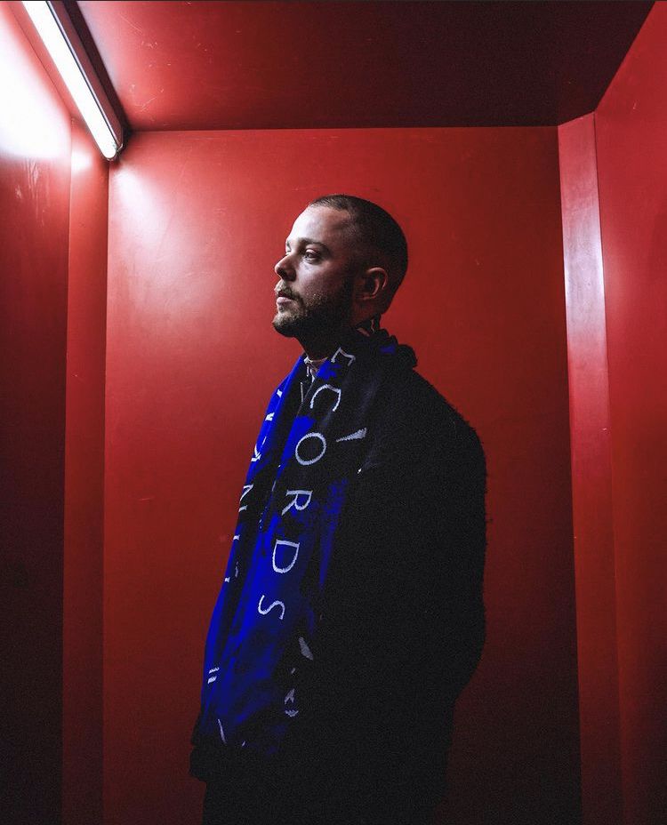 Man in a red room wearing a blue Pinkman Records scarf