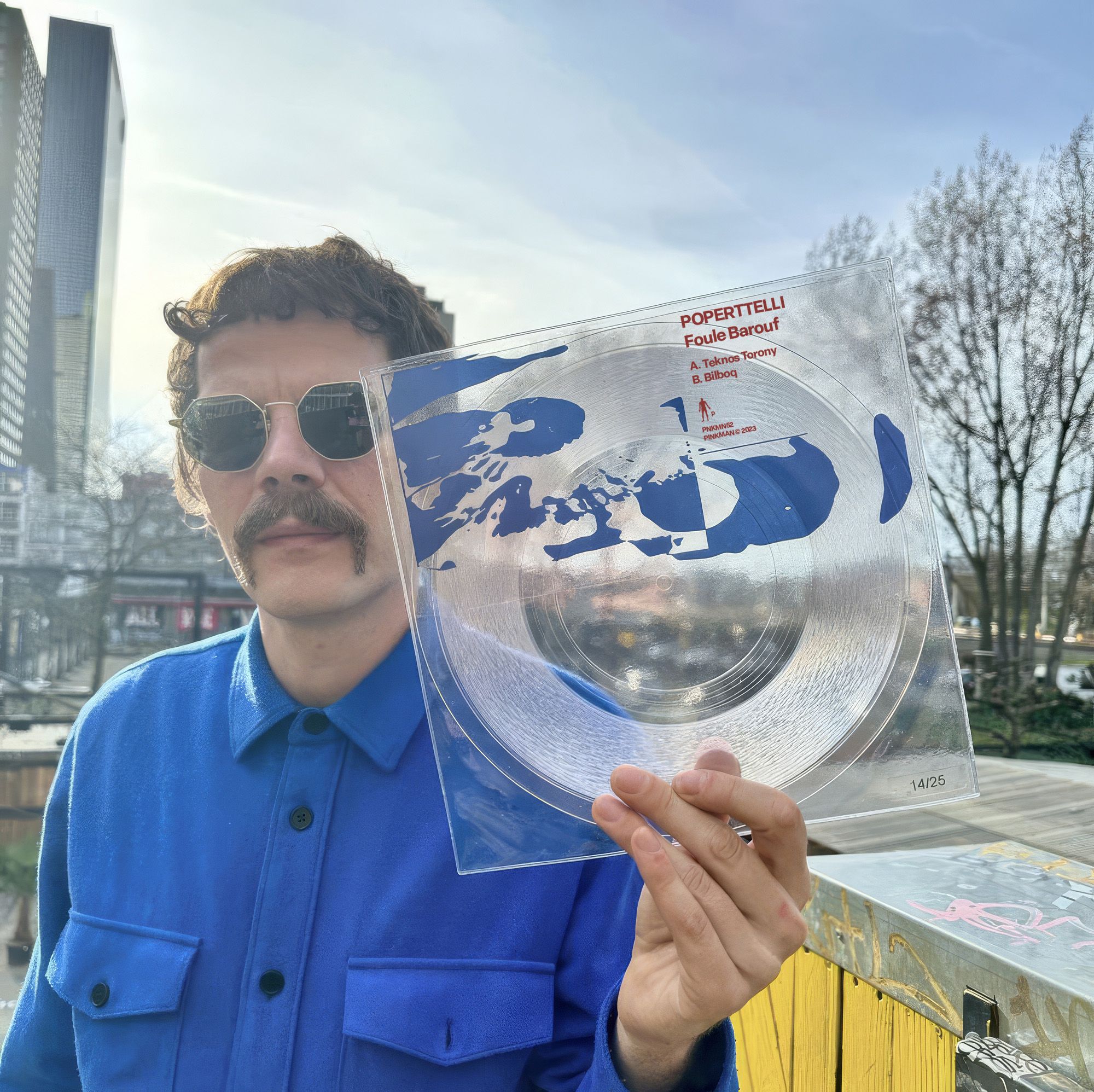 A man in sunglasses holding up a clear vinyl record with a blue sleeve outdoors