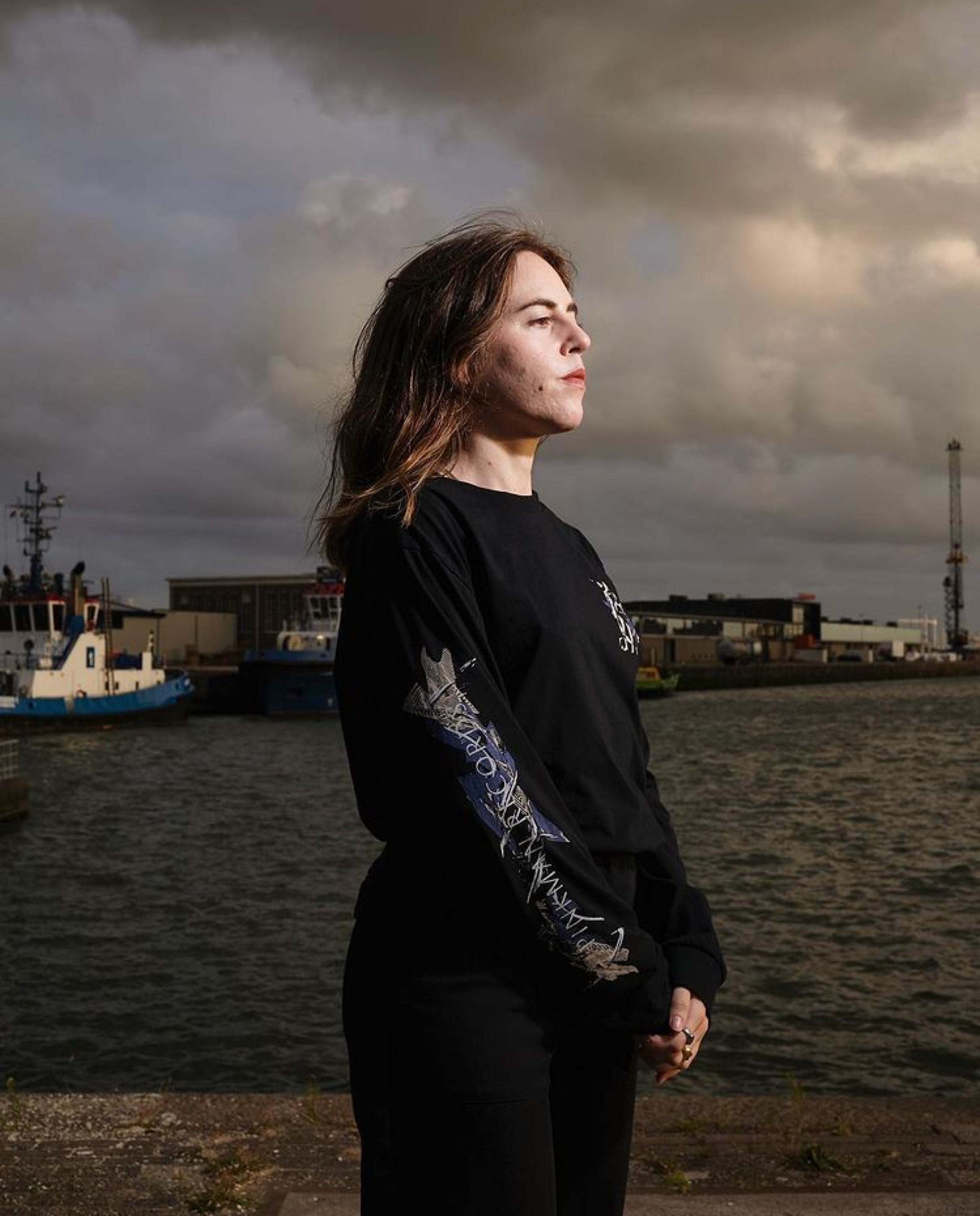 Woman in a black Pinkman long-sleeve shirt by a harbour