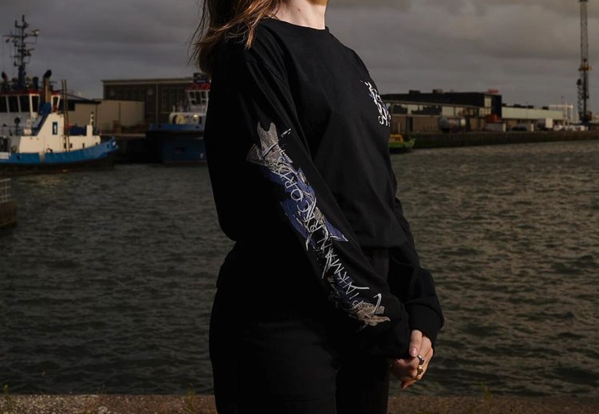 Woman in a black Pinkman long-sleeve shirt by a harbour