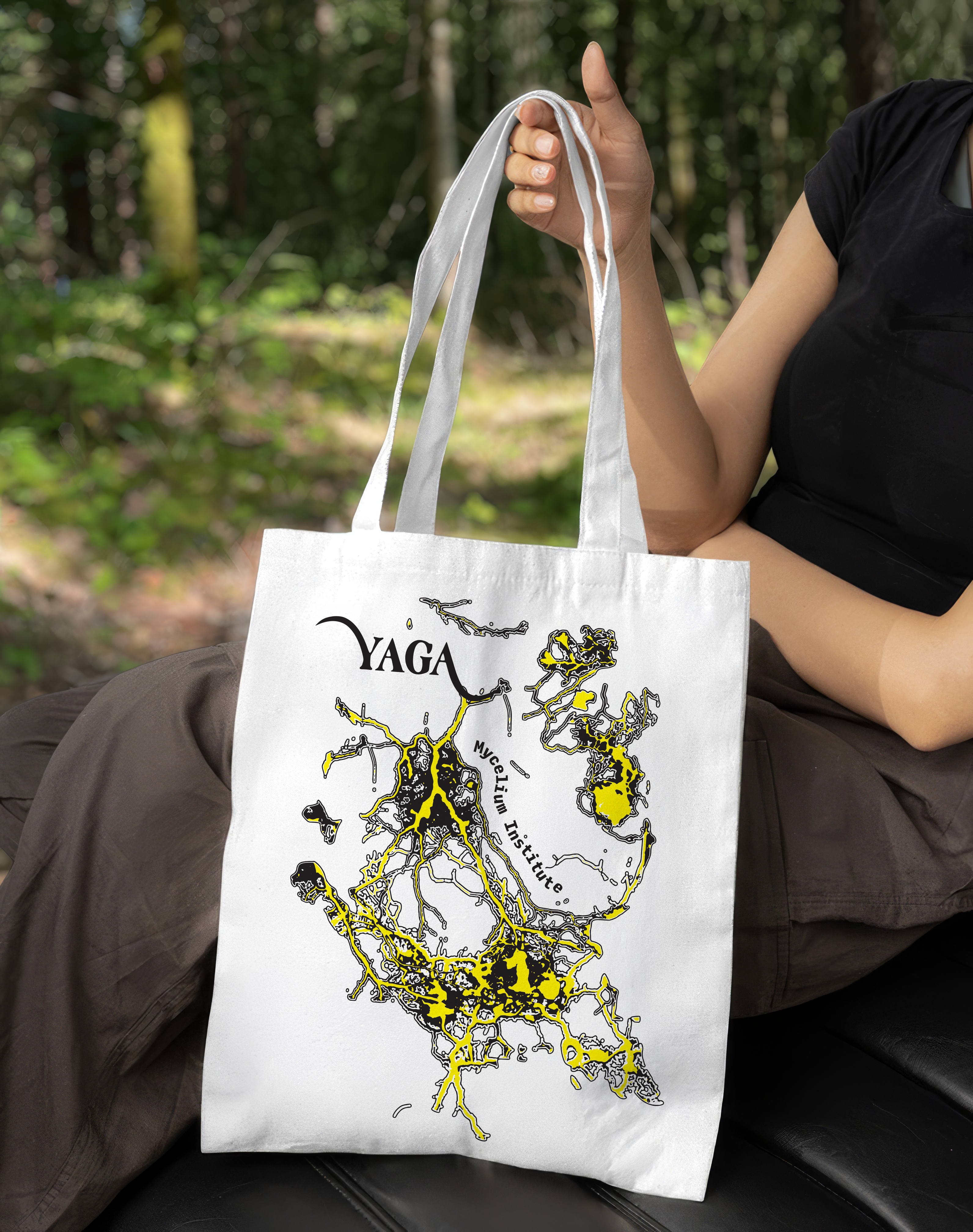 A person holding a white YAGA tote bag printed with black and yellow mycelium graphics