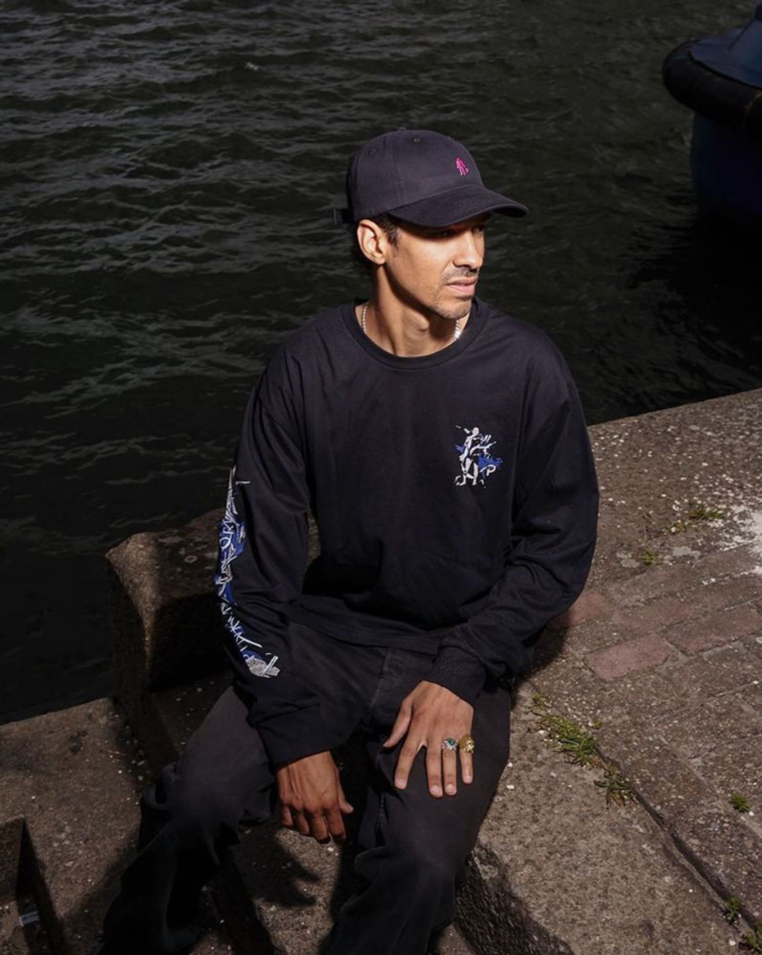 Person in a black long-sleeve shirt and cap sitting by the water