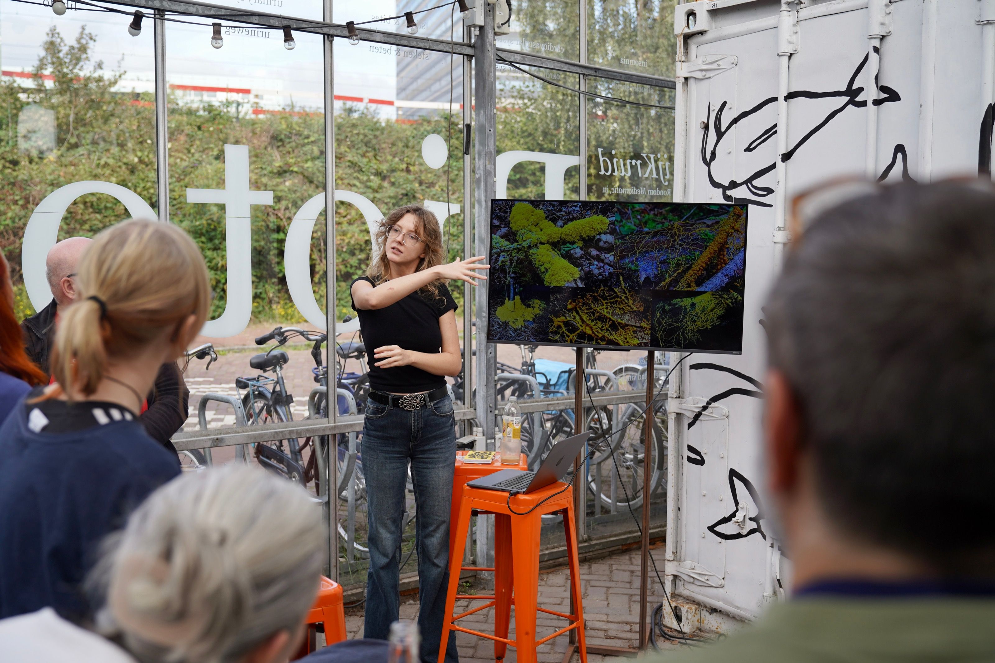 Speaker presenting slime mould visuals on a screen to an outdoor audience
