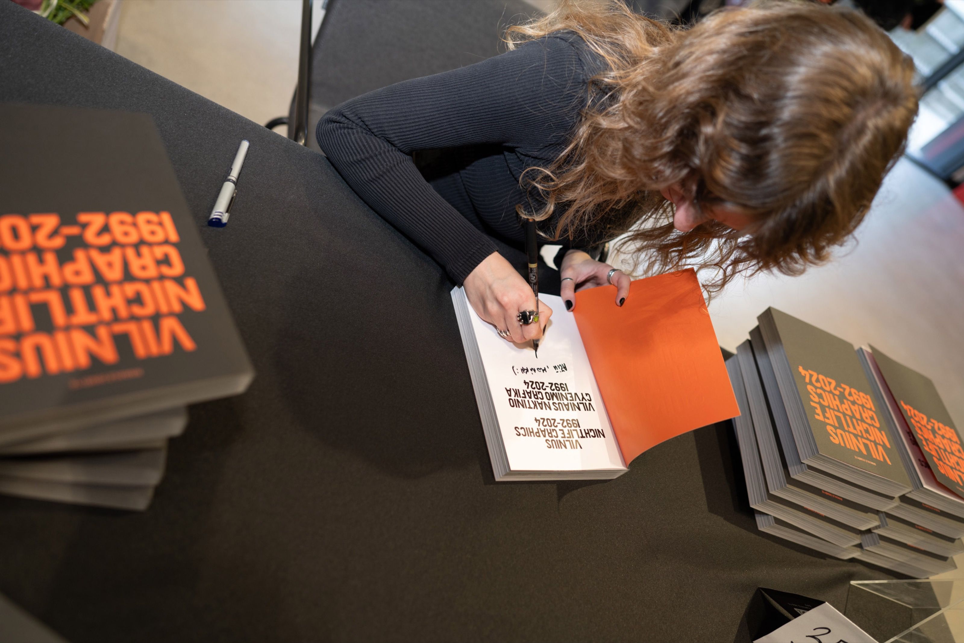 Close-up of a copy of Vilnius Nightlife Graphics 1992–2024 being signed
