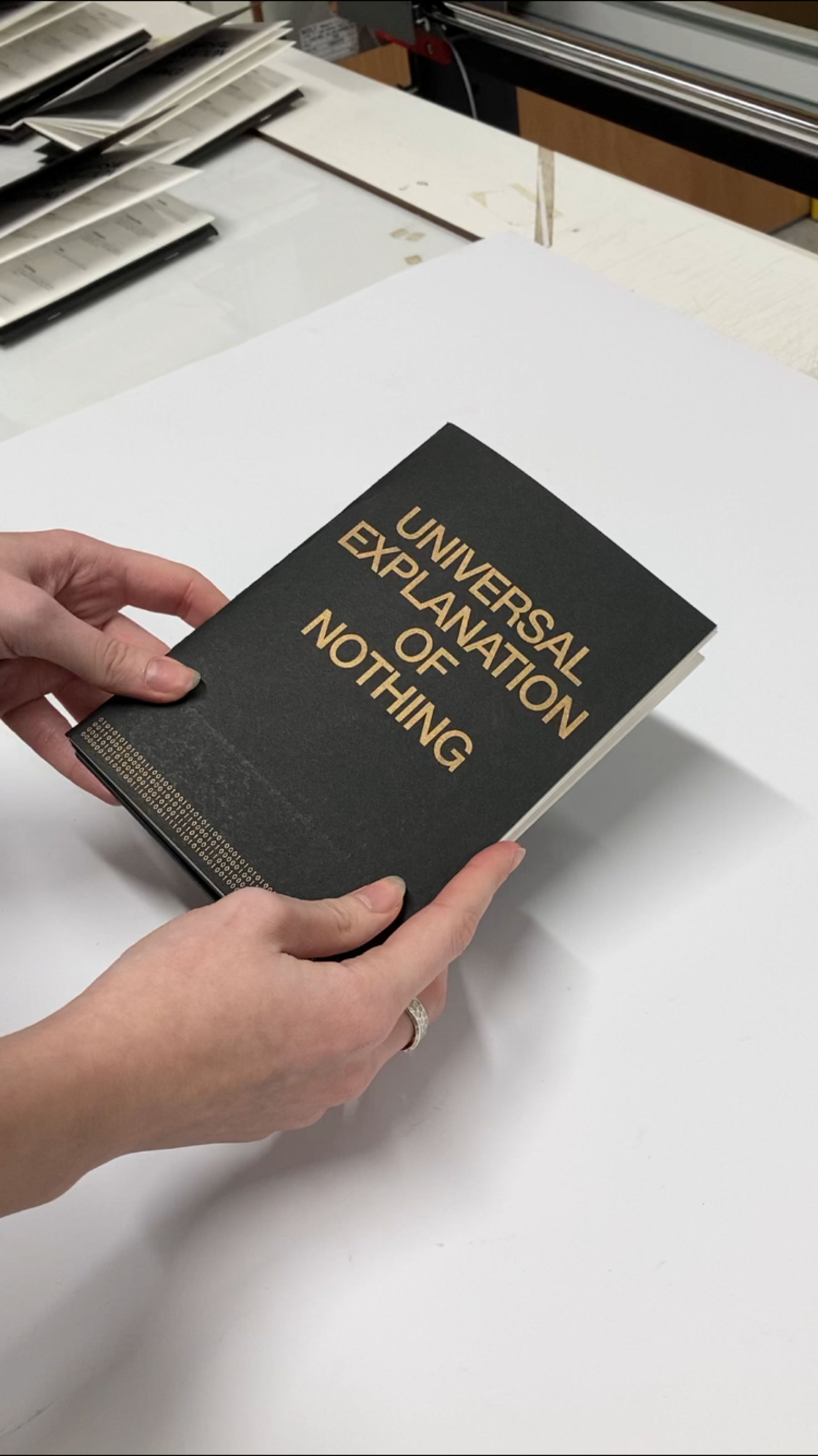 Hands holding the Universal Explanation of Nothing book with gold title on black
