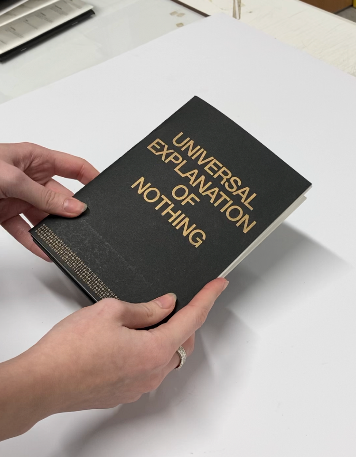 Hands holding the Universal Explanation of Nothing book with gold title on black