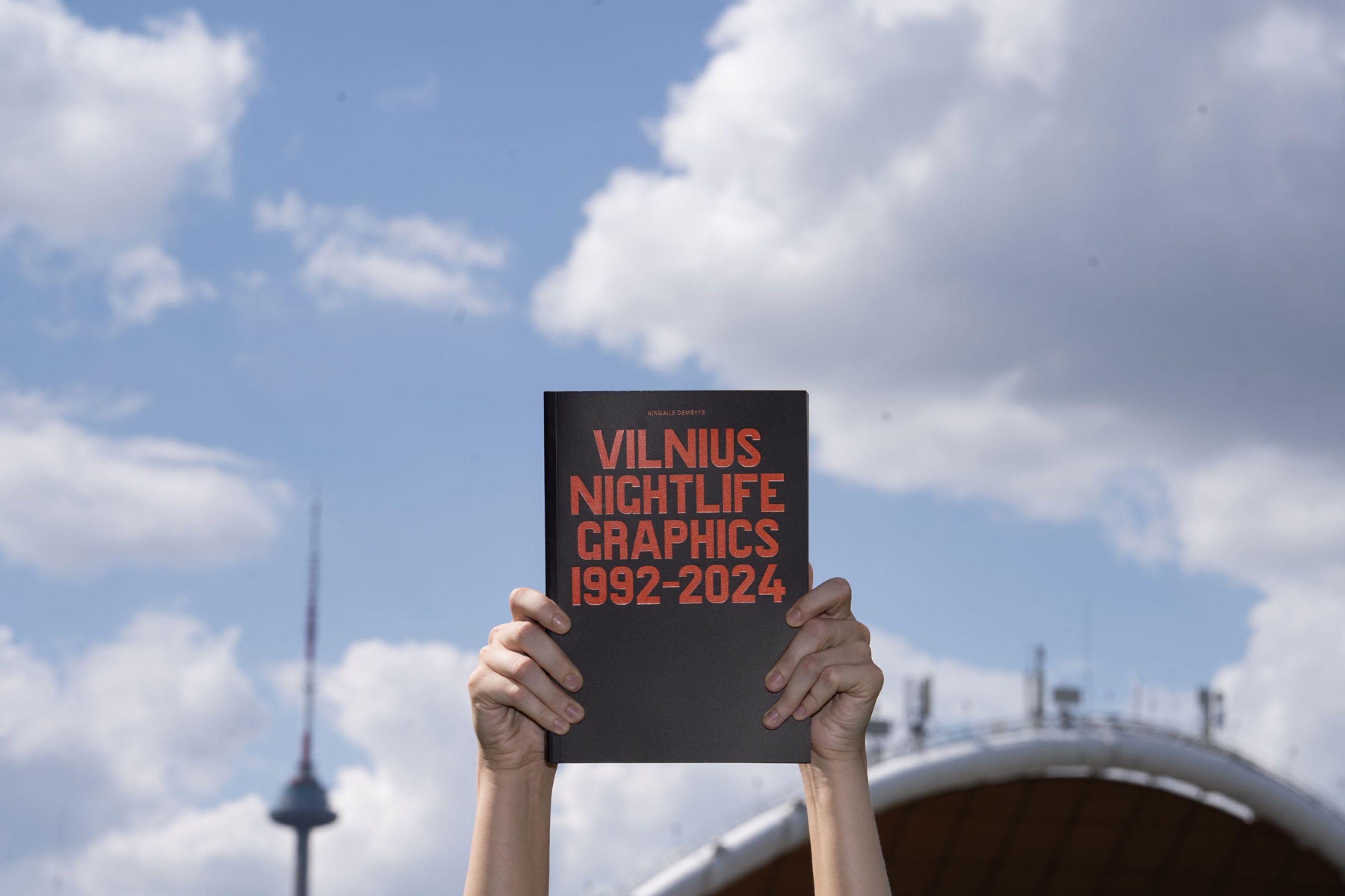 Hands holding Vilnius Nightlife Graphics 1992–2024 against the sky