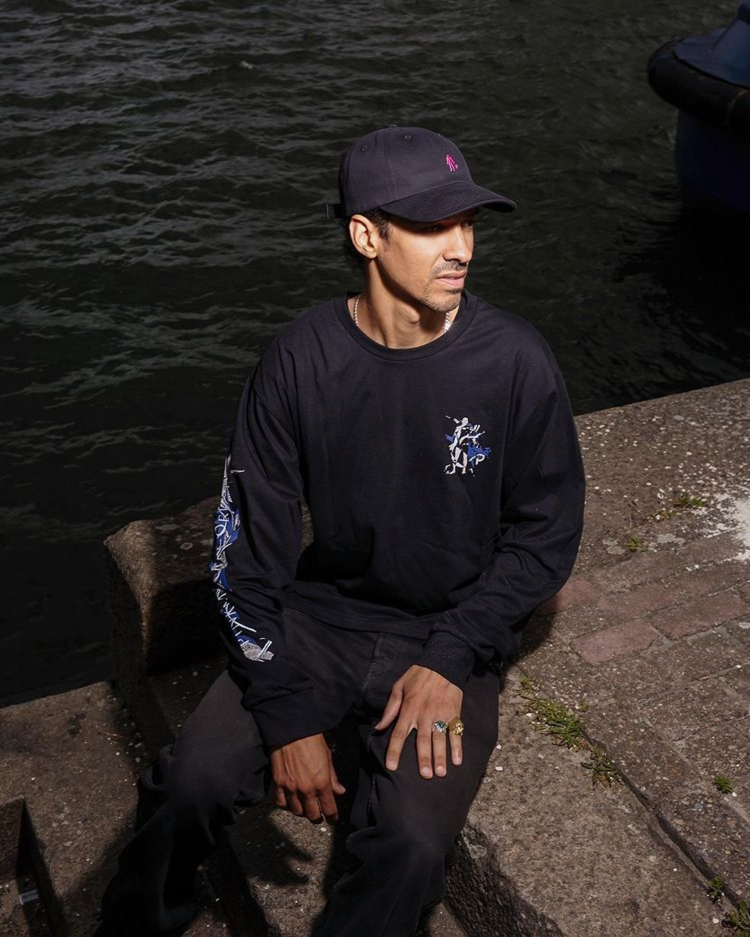 Man in a Pinkman long-sleeve shirt and cap by the water