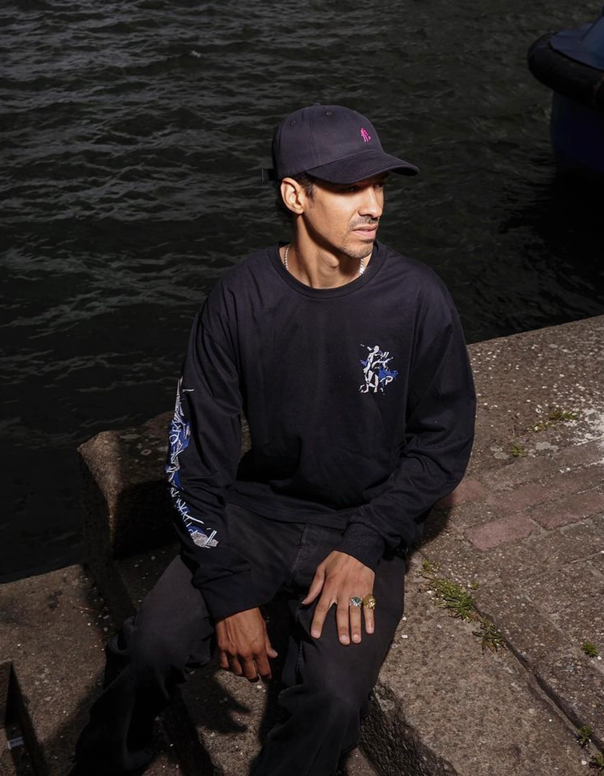 Man in a Pinkman long-sleeve shirt and cap by the water