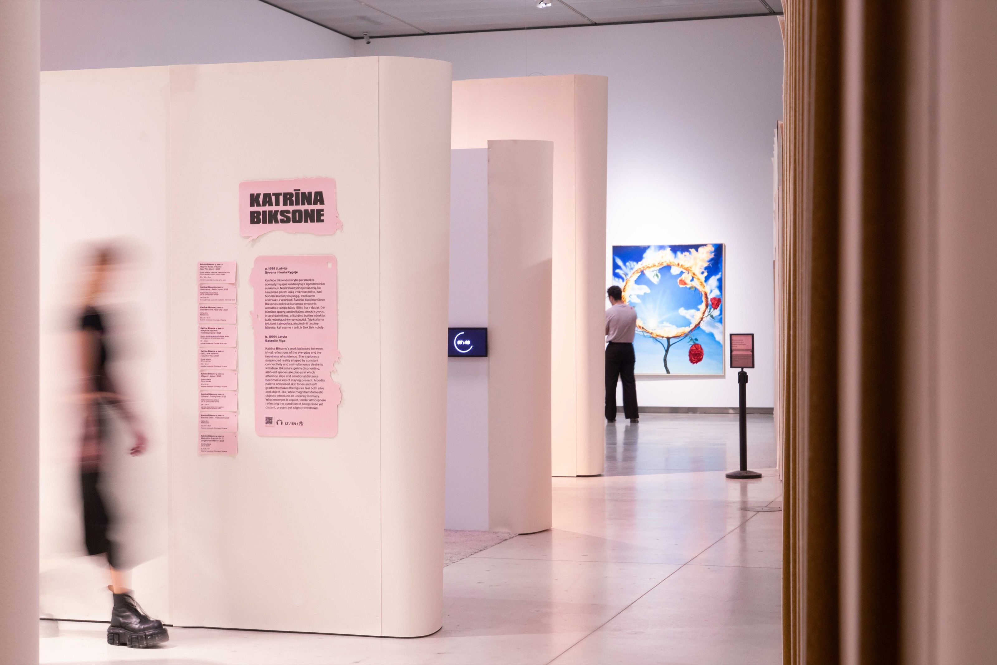 Visitor walking past a pink artist text panel, Gen Z. All at Once