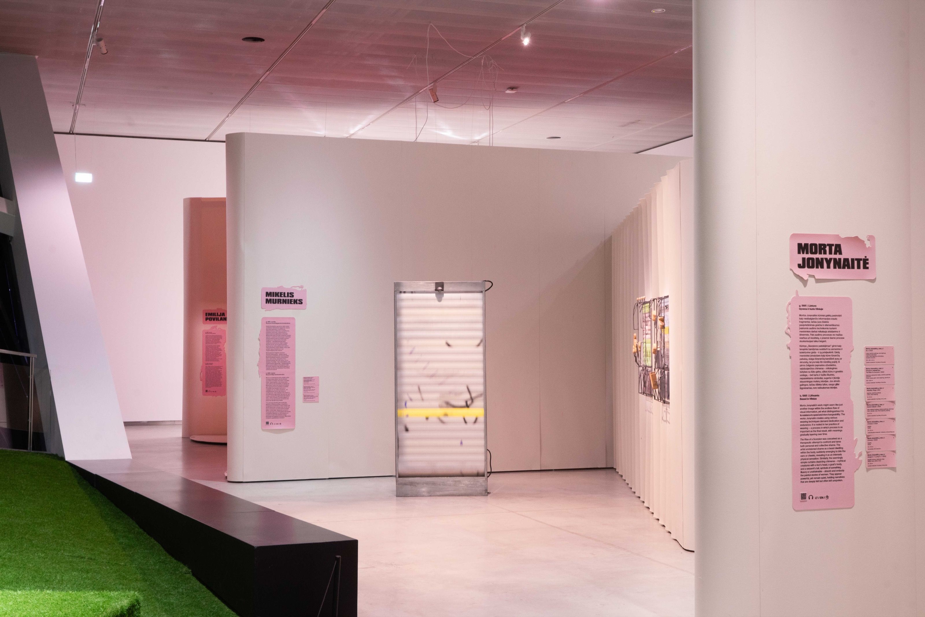 Exhibition rooms with pink artist texts and green floor islands, MO Museum