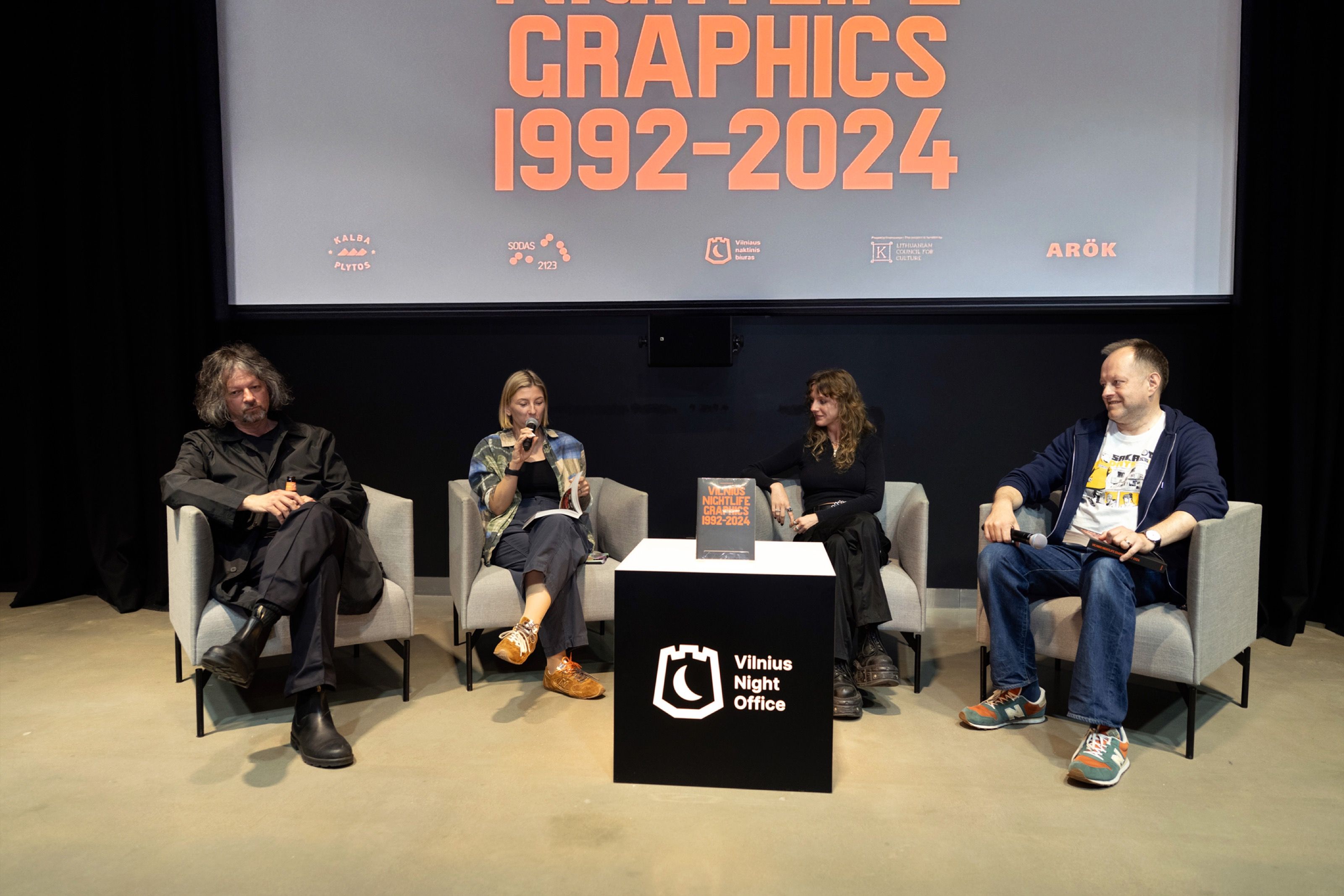 Panel discussion on stage under a Vilnius Nightlife Graphics 1992–2024 screen