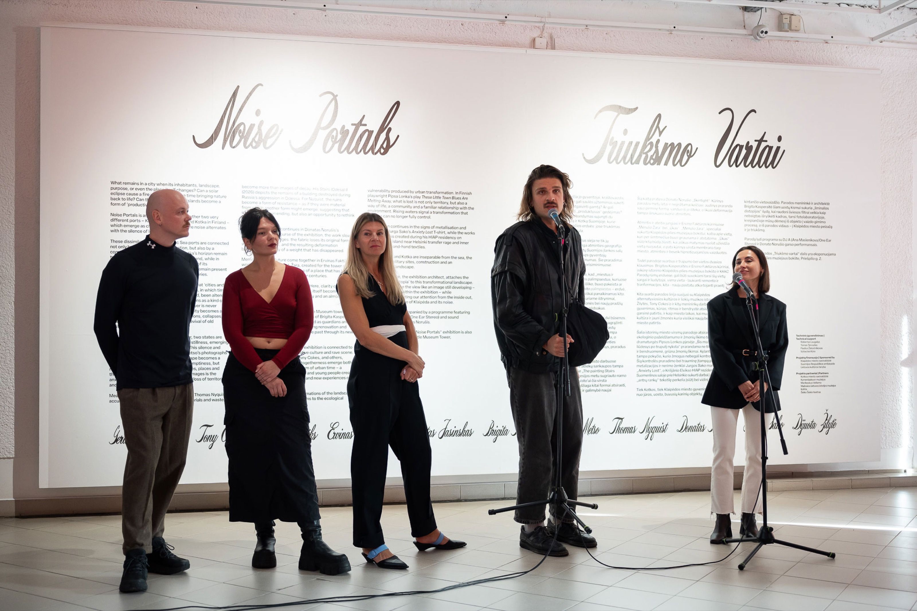 Curators and artists speaking at the Noise Portals opening in front of the title wall