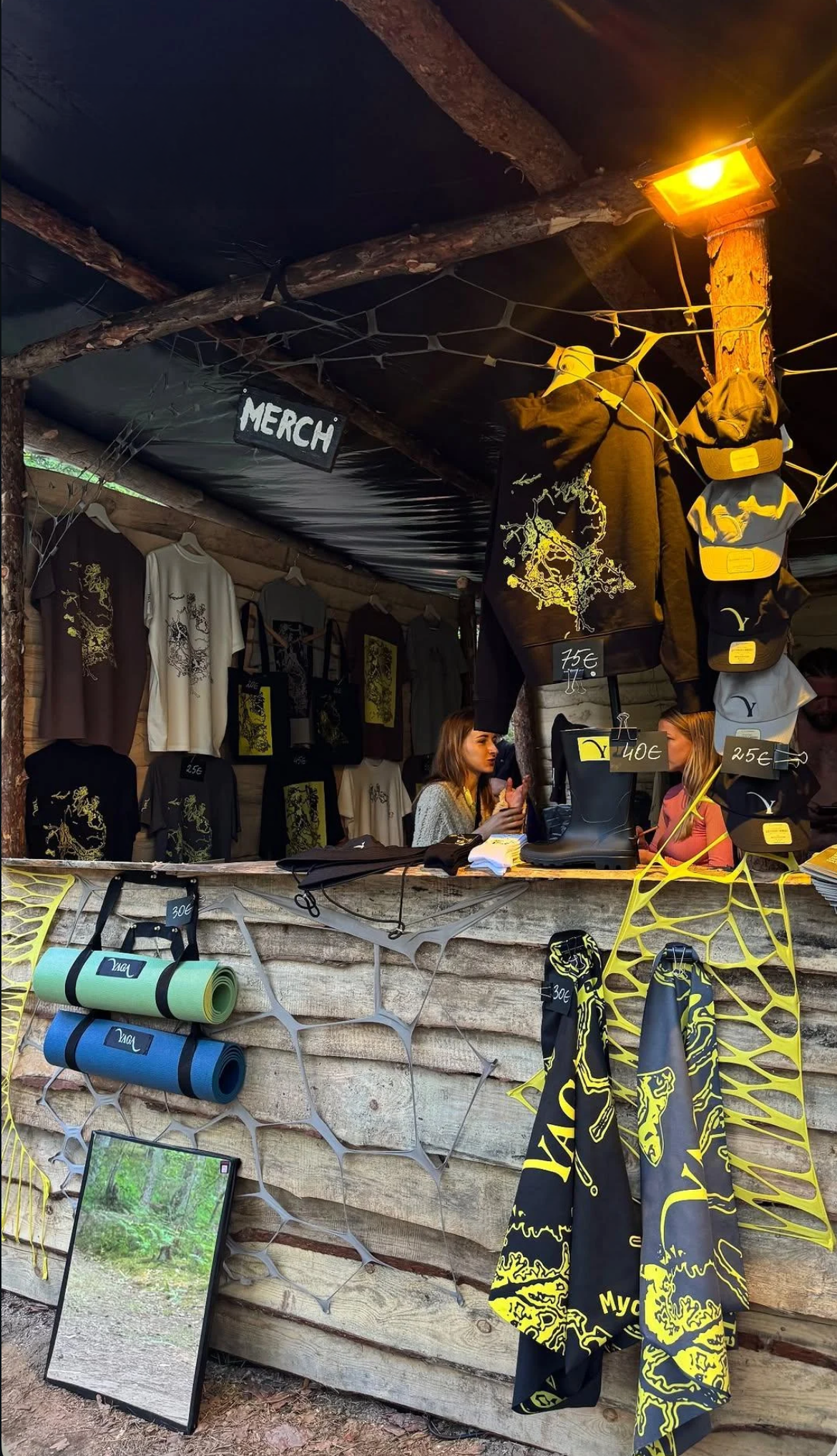 The YAGA merch stand at the festival, with T-shirts and bags hanging on a wooden stall