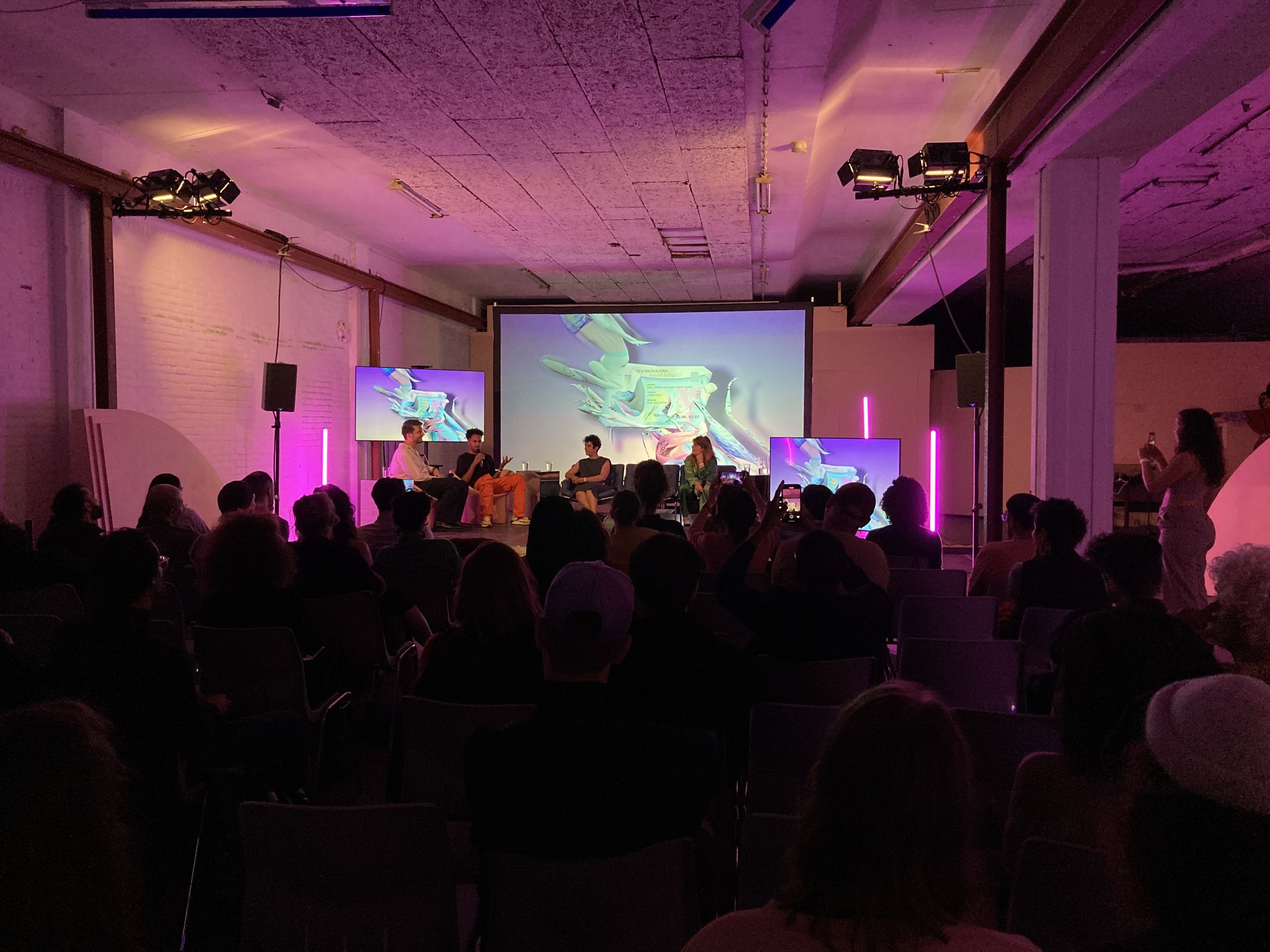 Audience at a New Radicalisms event in a pink-lit hall