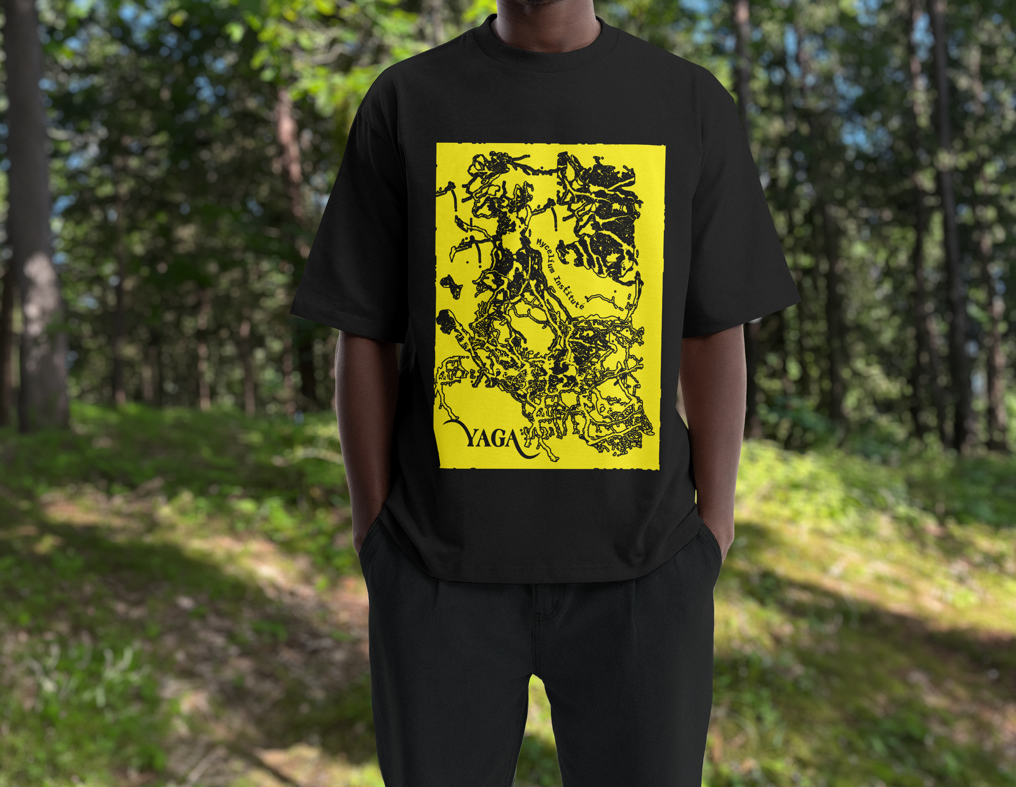 A person in a forest wearing a black YAGA T-shirt with a yellow print