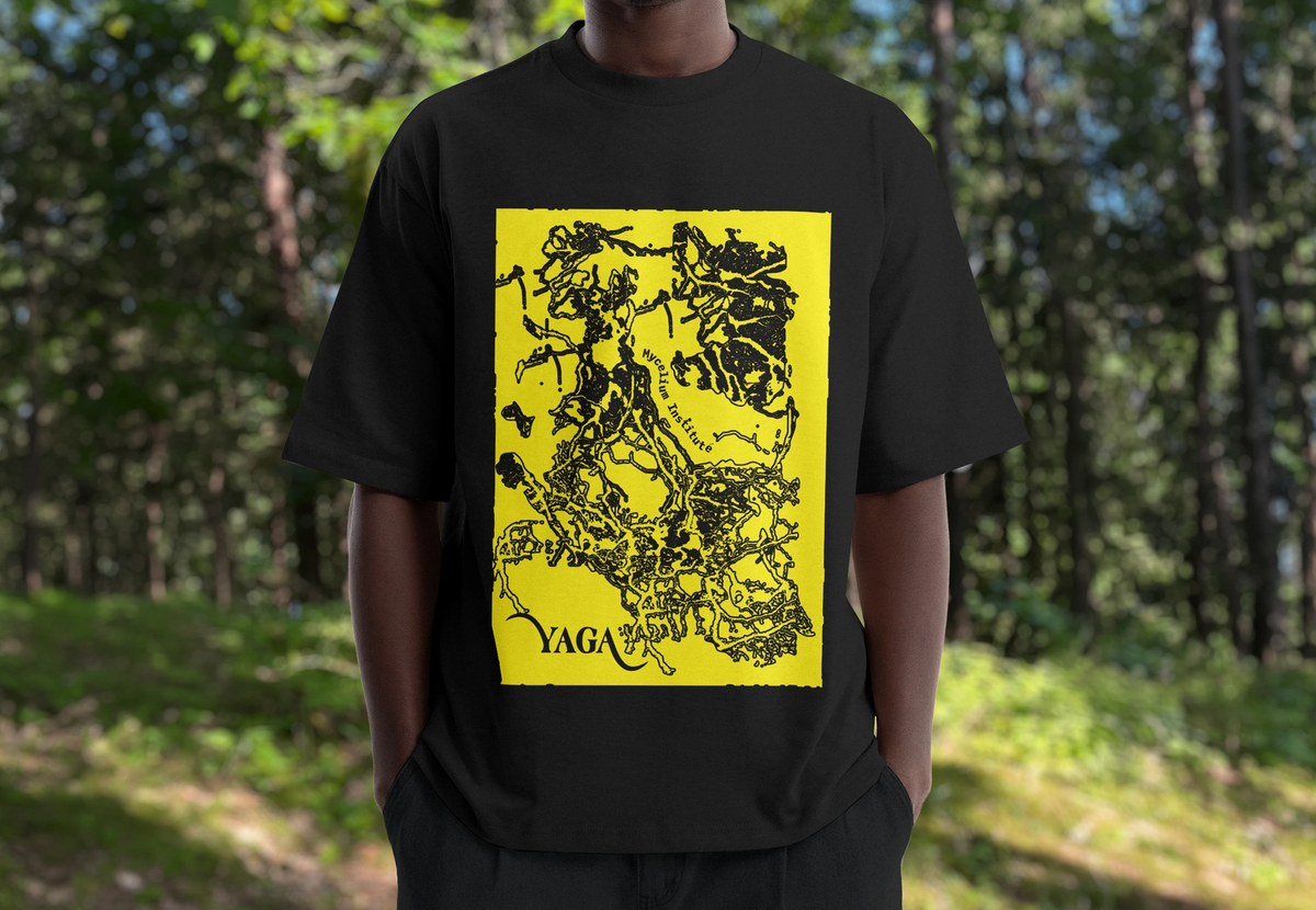 A person in a forest wearing a black YAGA T-shirt with a yellow print