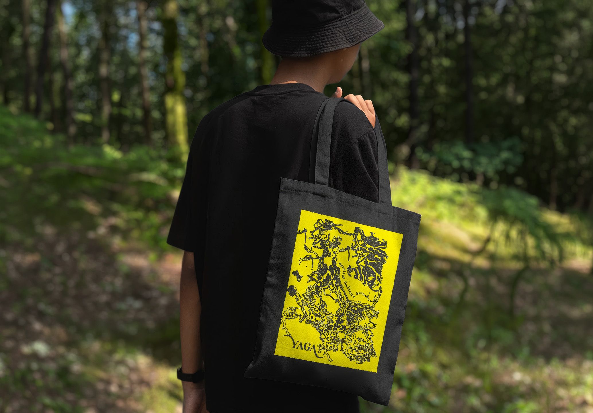 A person in a forest carrying a black YAGA tote bag with a yellow print