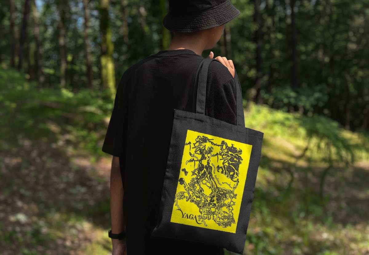 A person in a forest carrying a black YAGA tote bag with a yellow print