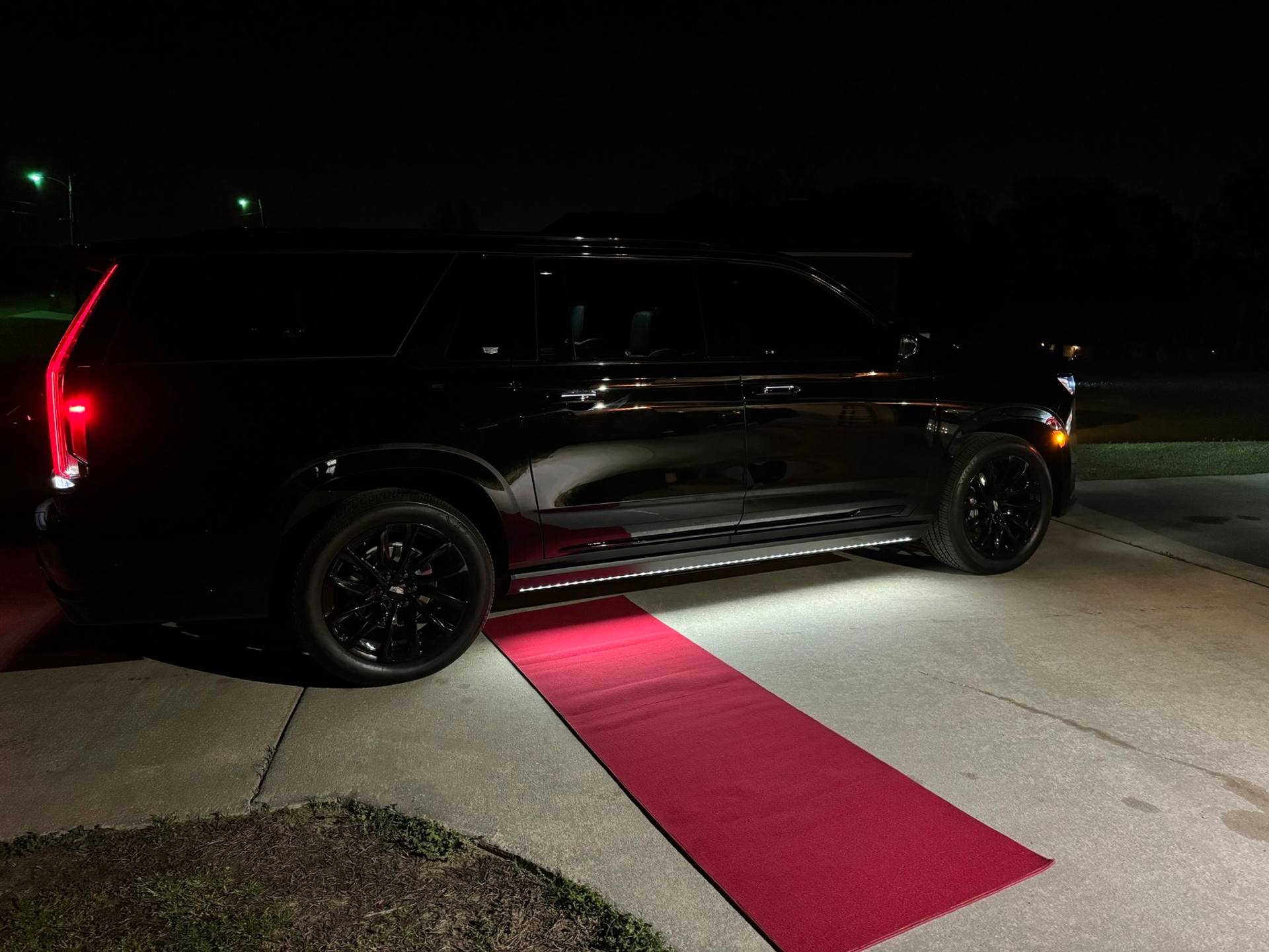 A black Cadillac Escalade waiting on a red carpet at night