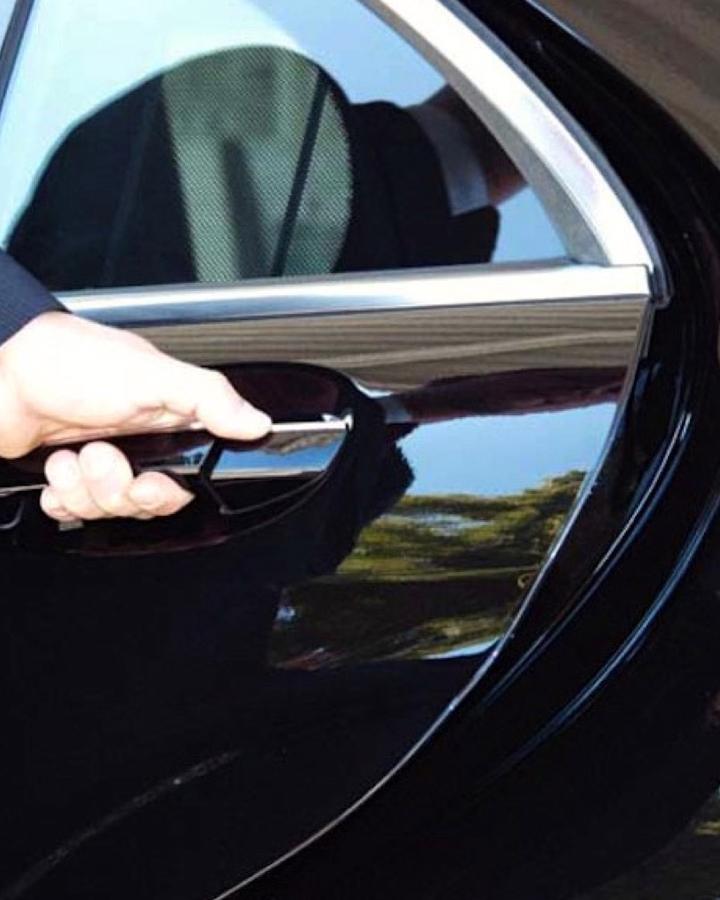 A chauffeur opening the rear door of a black sedan