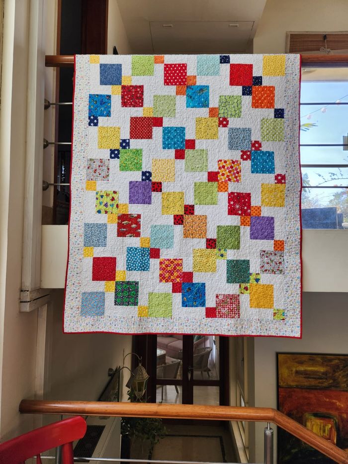 Rainbow scrappy quilt hung flat, showing the full patchwork of colourful squares