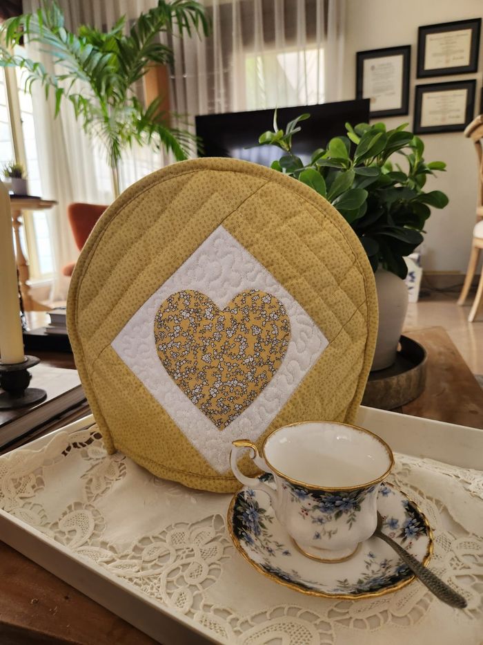 Mustard-gold quilted tea cosy with a floral appliqué heart on a white diamond