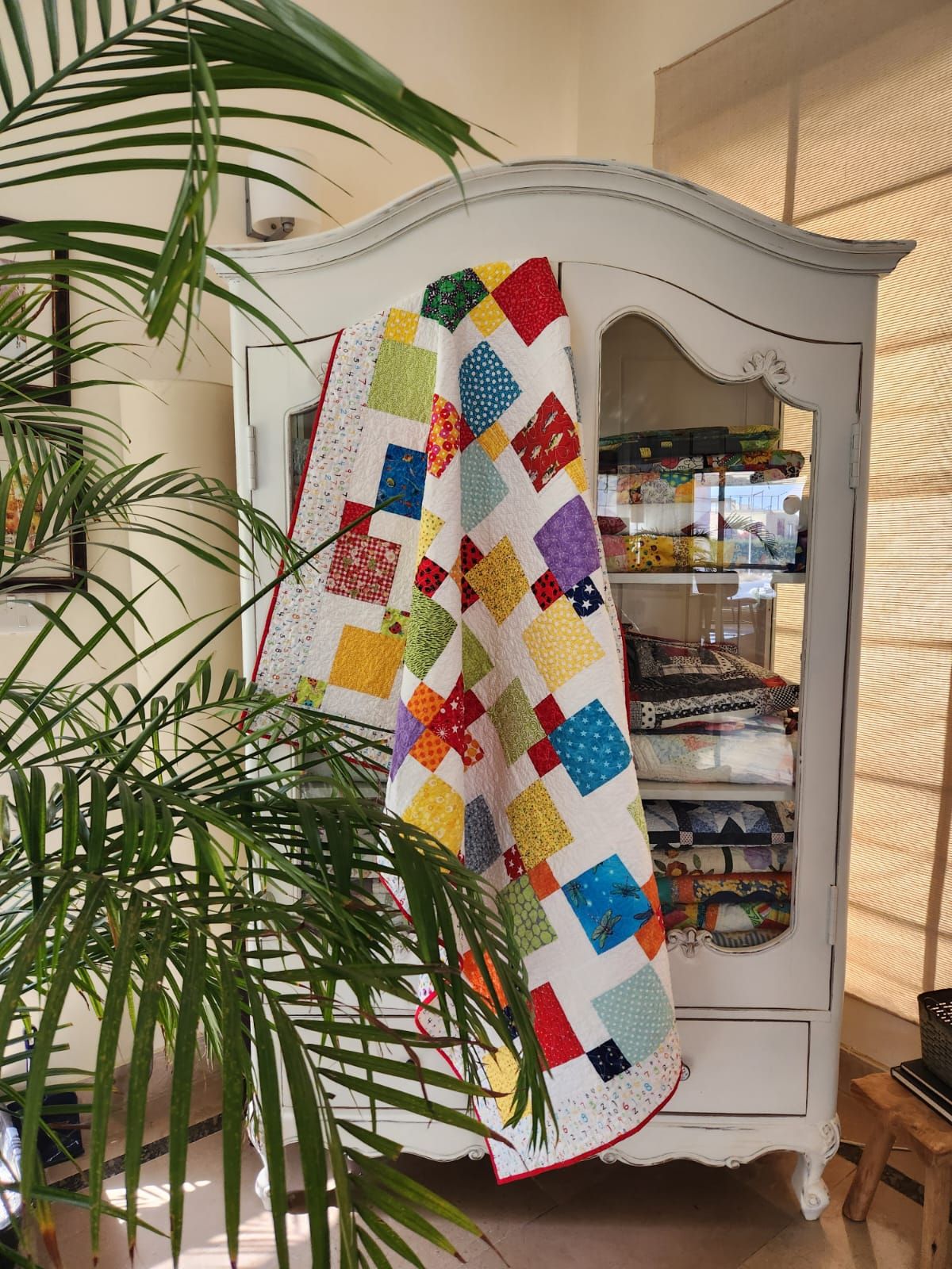 Rainbow scrappy quilt draped over a painted armoire