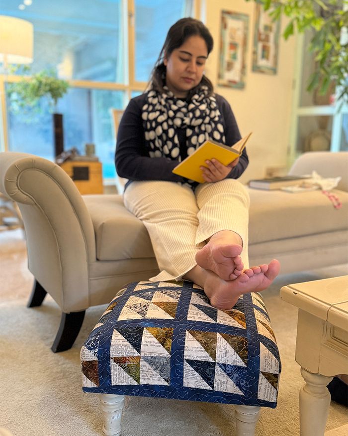 Navy patchwork upholstered footstool in use beside a sofa