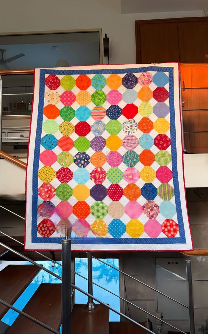 Rainbow dots quilt hung flat, showing the full pattern of scrappy coloured dots