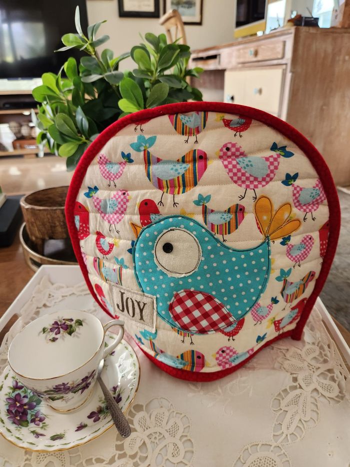 Brightly coloured tea cosy with a large turquoise appliqué bird and a JOY label