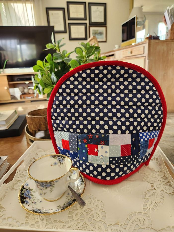 Navy polka dot tea cosy with a pieced band of red and blue scrap squares and red binding