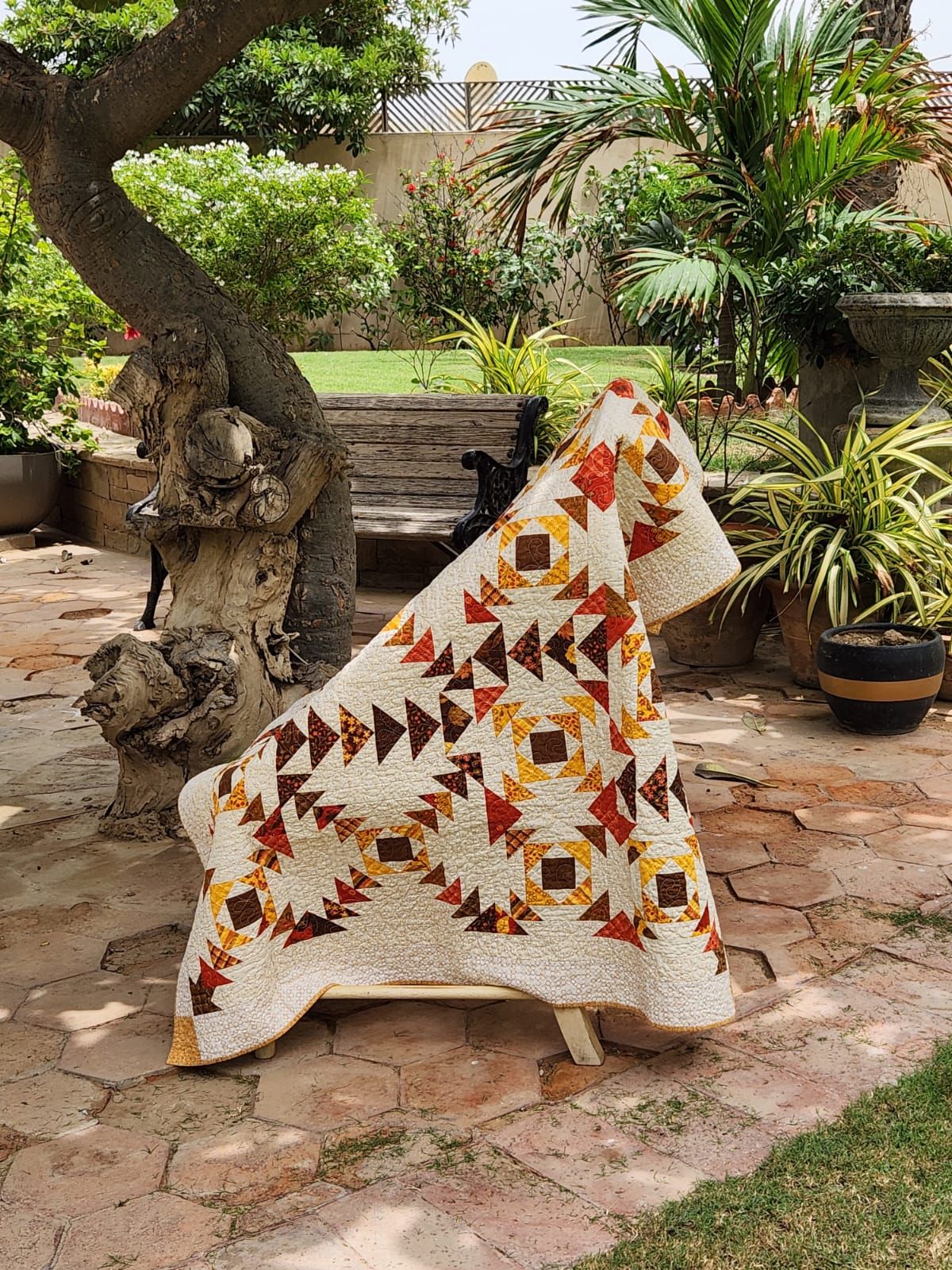 Autumn flying geese lap quilt draped over a garden bench