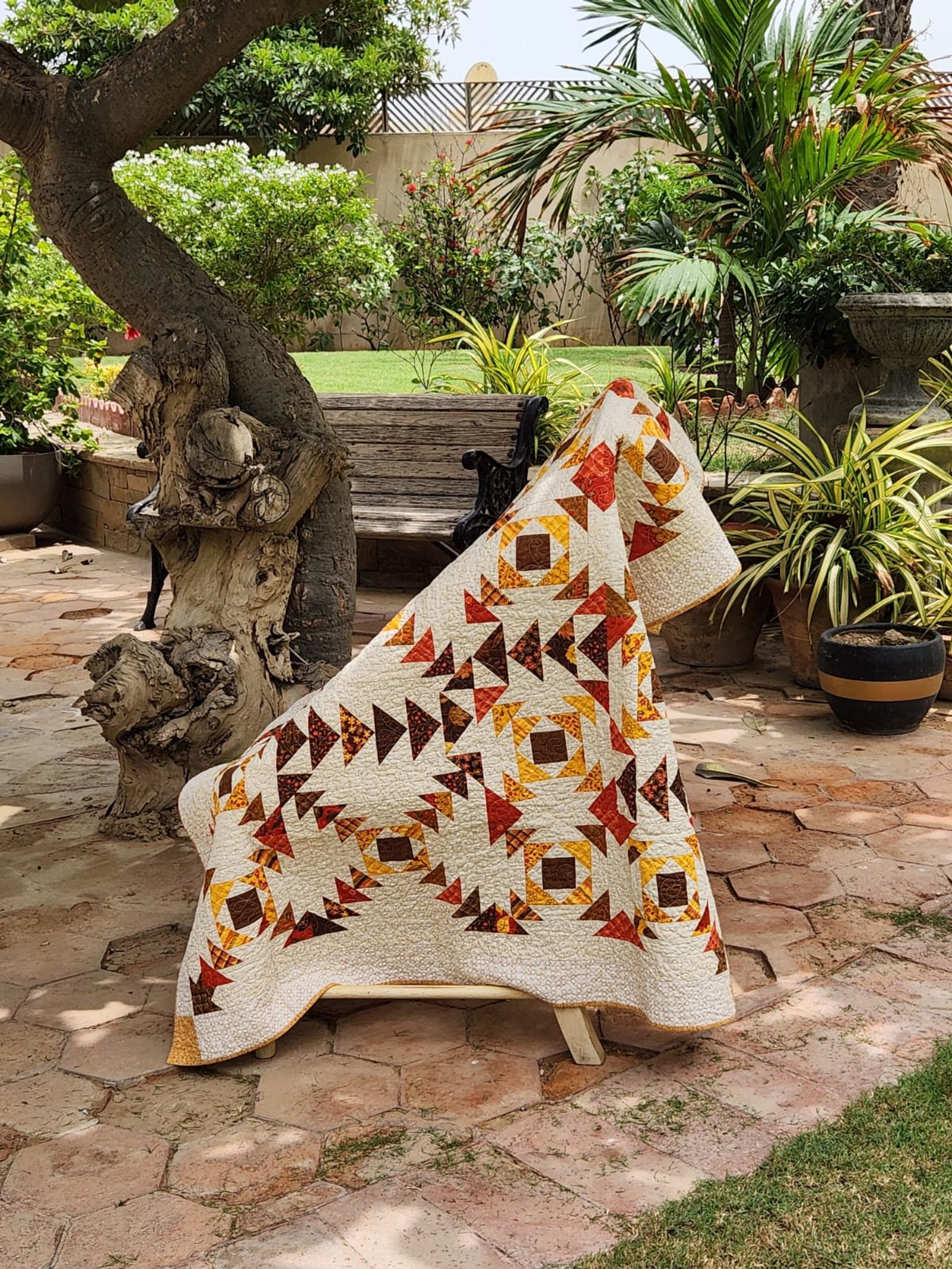 Autumn flying geese lap quilt draped over a garden bench
