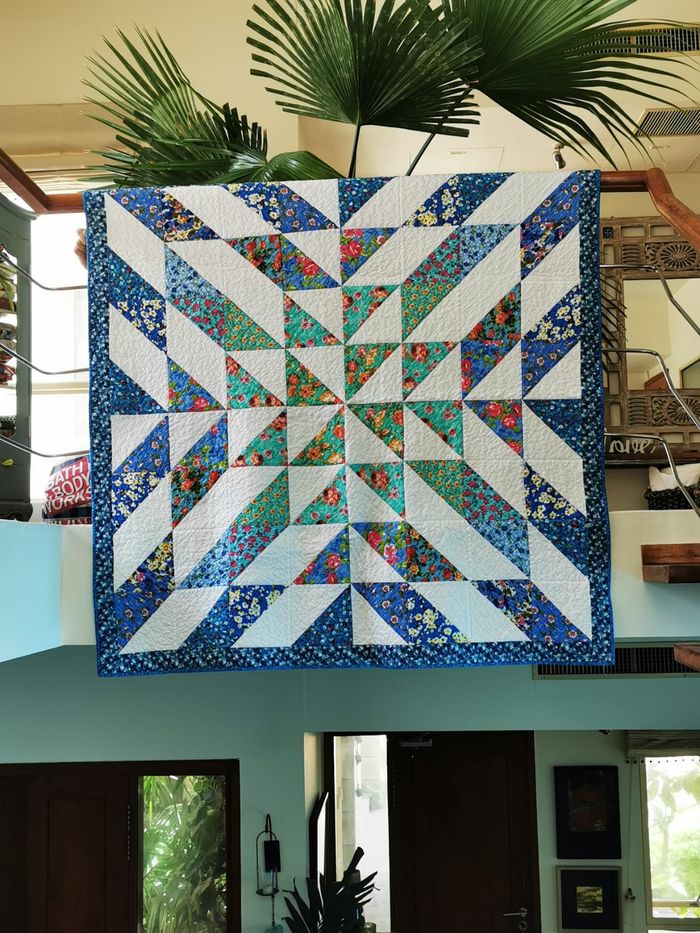Radiant star lap quilt hung flat, showing the full star pieced in blues, greens and florals