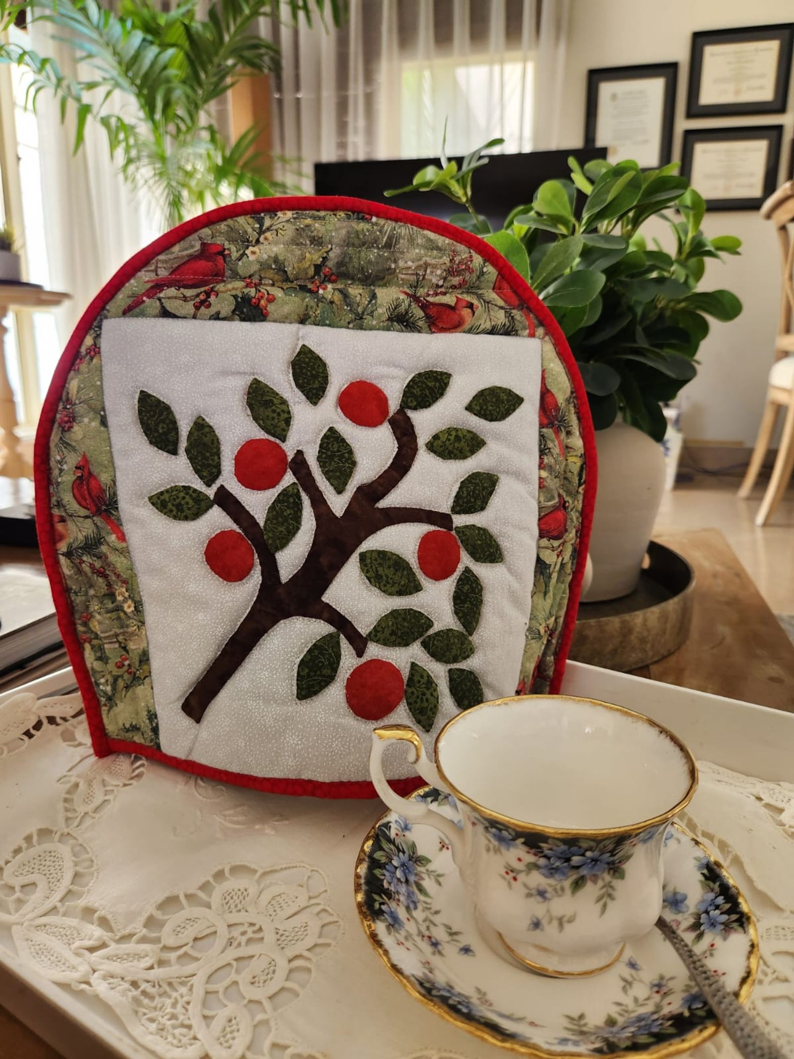 Tea cosy with an appliqué apple tree on cream, framed by woodland fabric with red binding