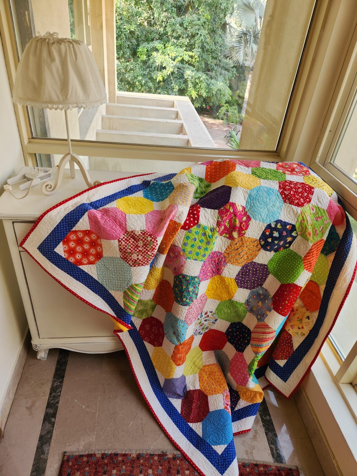 Rainbow dots quilt draped by a sunlit window