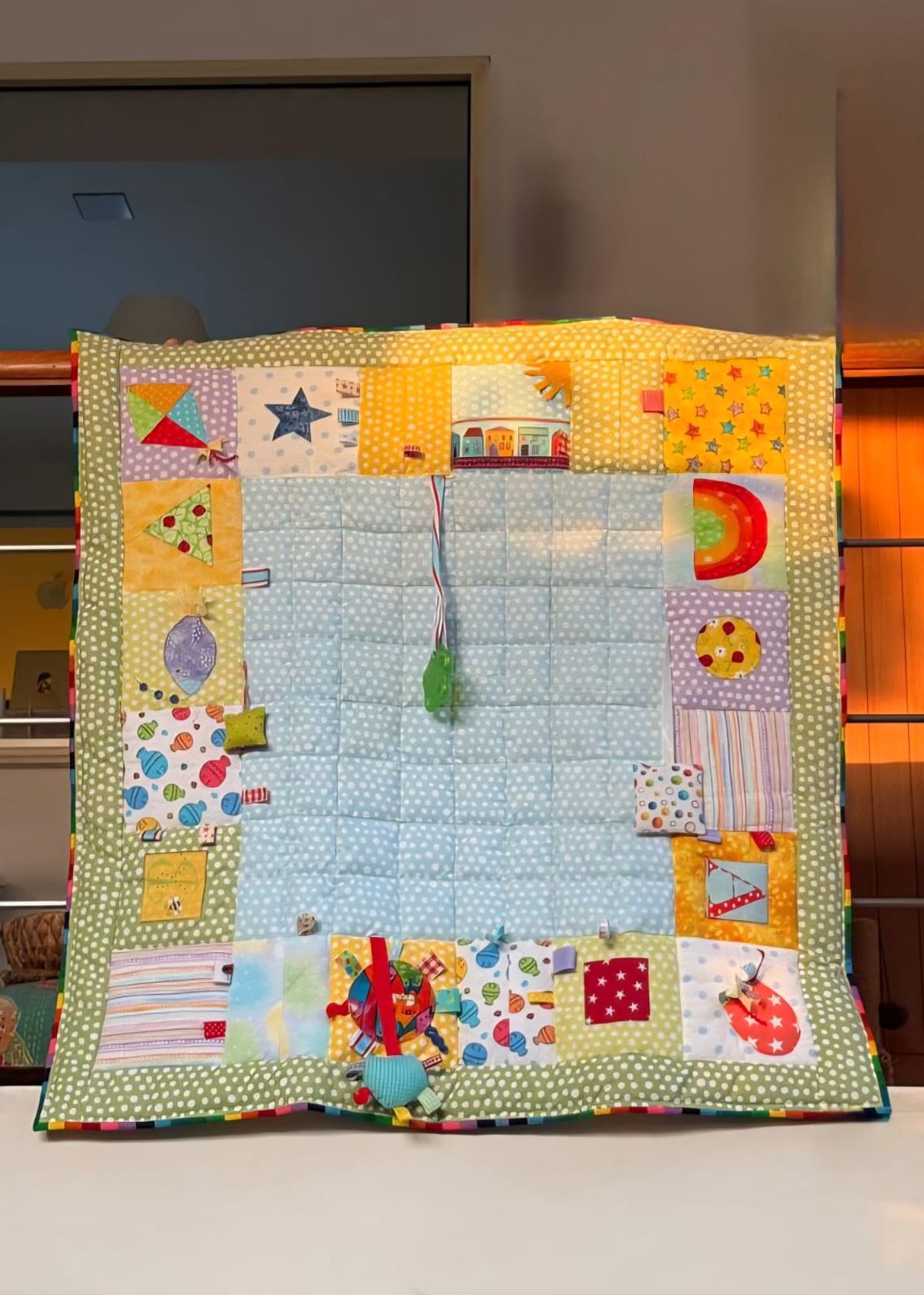Baby sensory playmat laid flat, showing the appliqué border of kites, stars, houses and rainbows