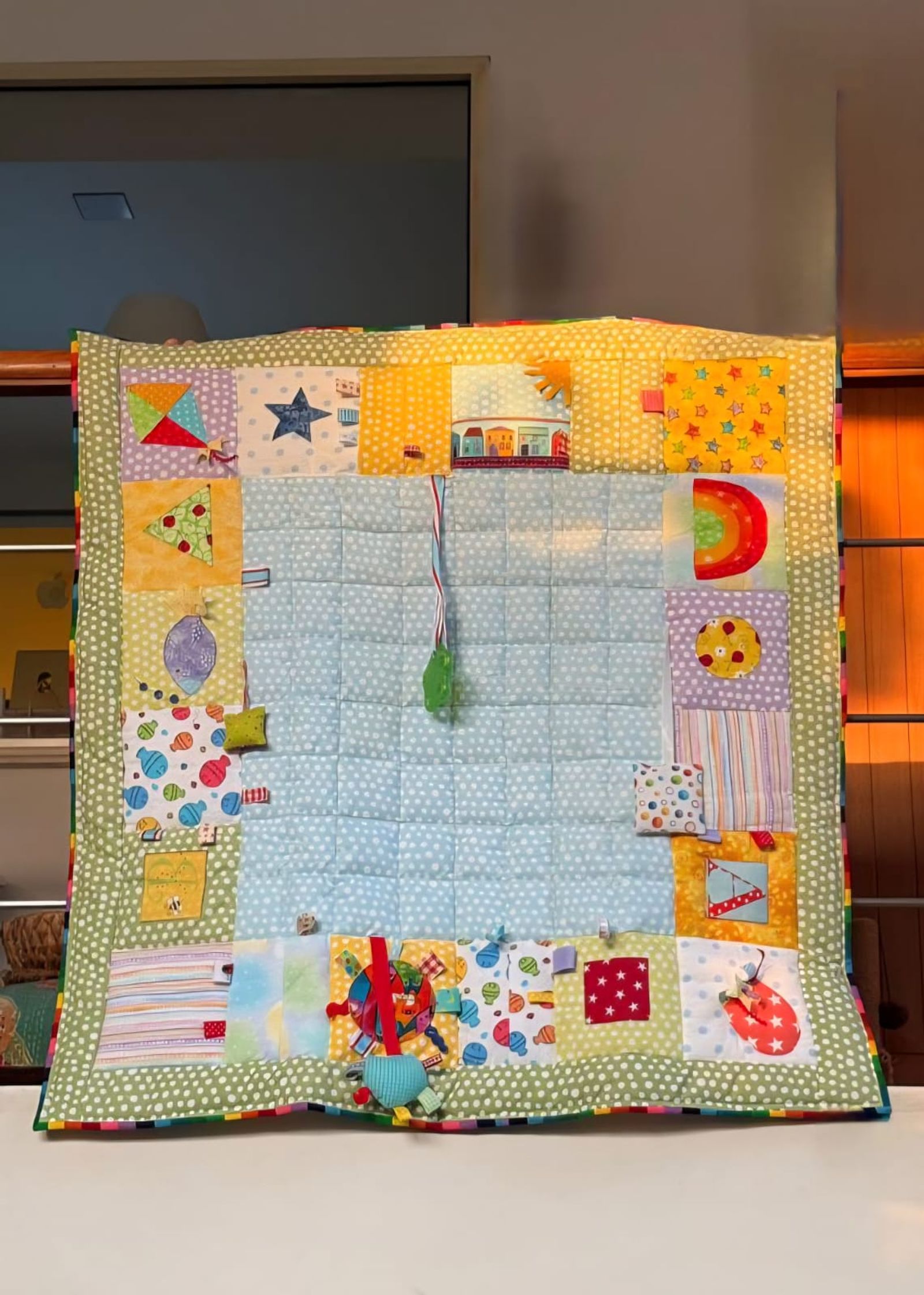 Baby sensory playmat laid flat, showing the appliqué border of kites, stars, houses and rainbows
