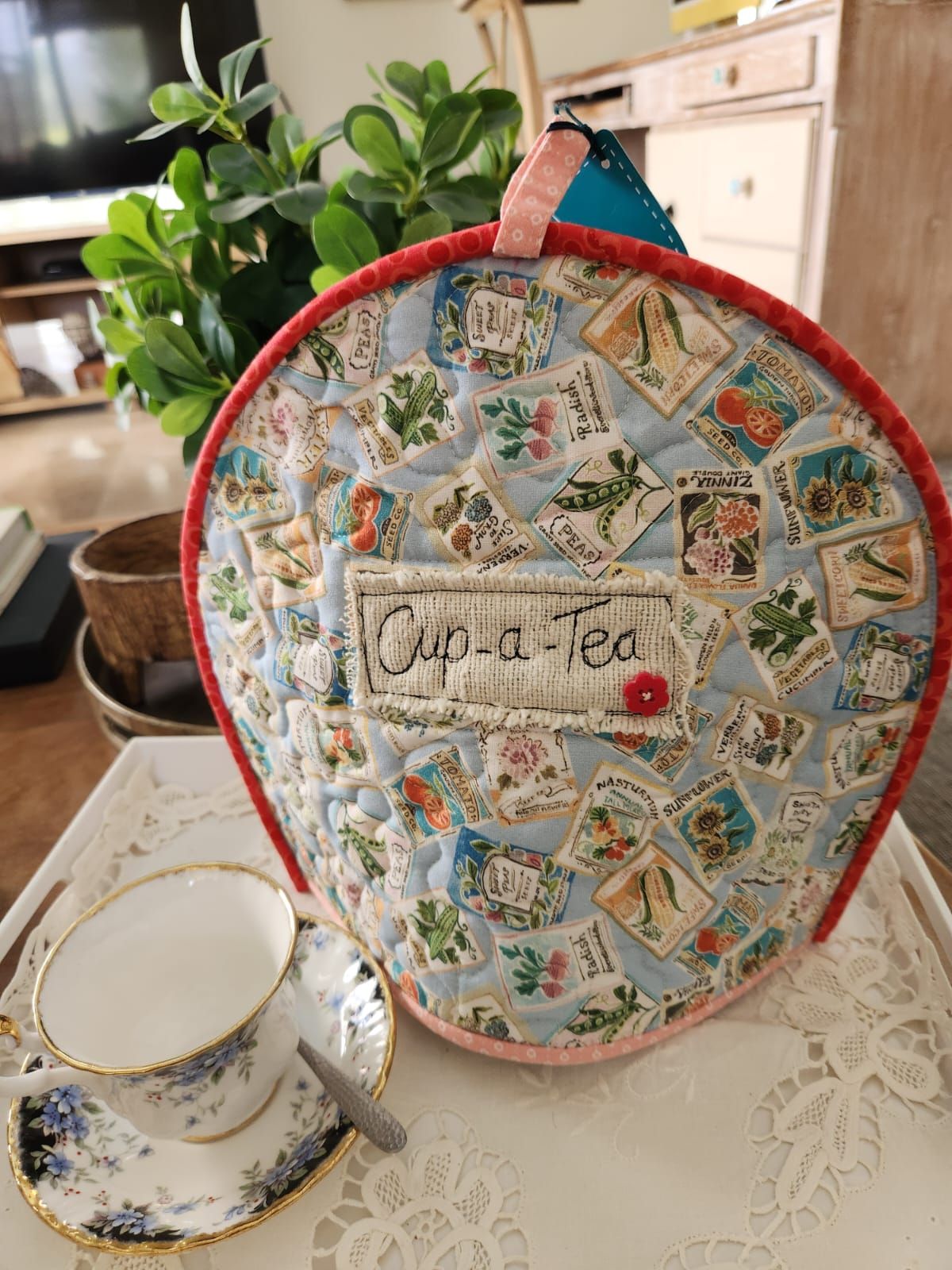 Back of the same tea cosy: a Cup-a-Tea linen tag with a red button on seed-packet fabric