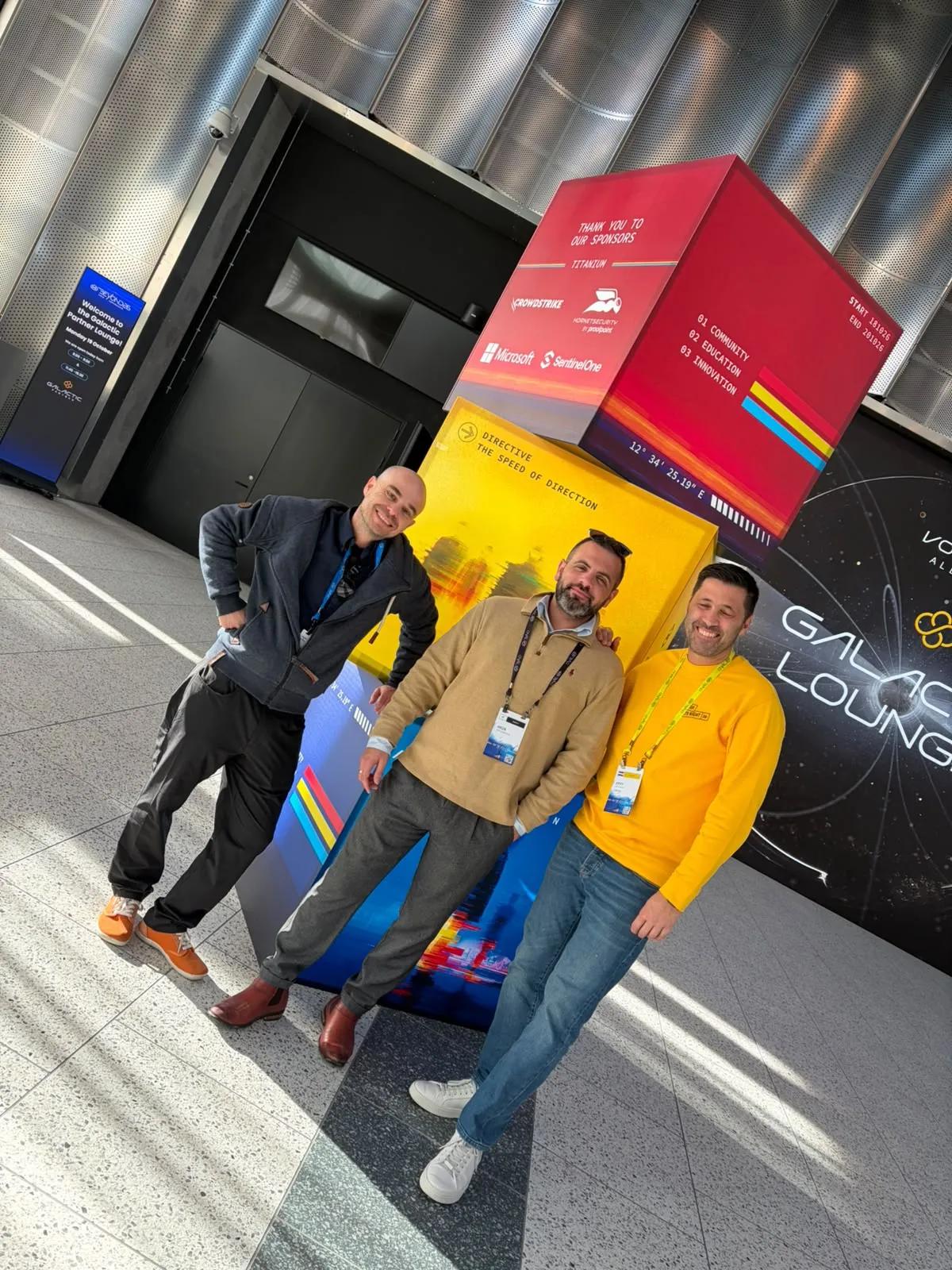 Three men with Pax8 Beyond badges laughing in front of the sponsor cube in the hall