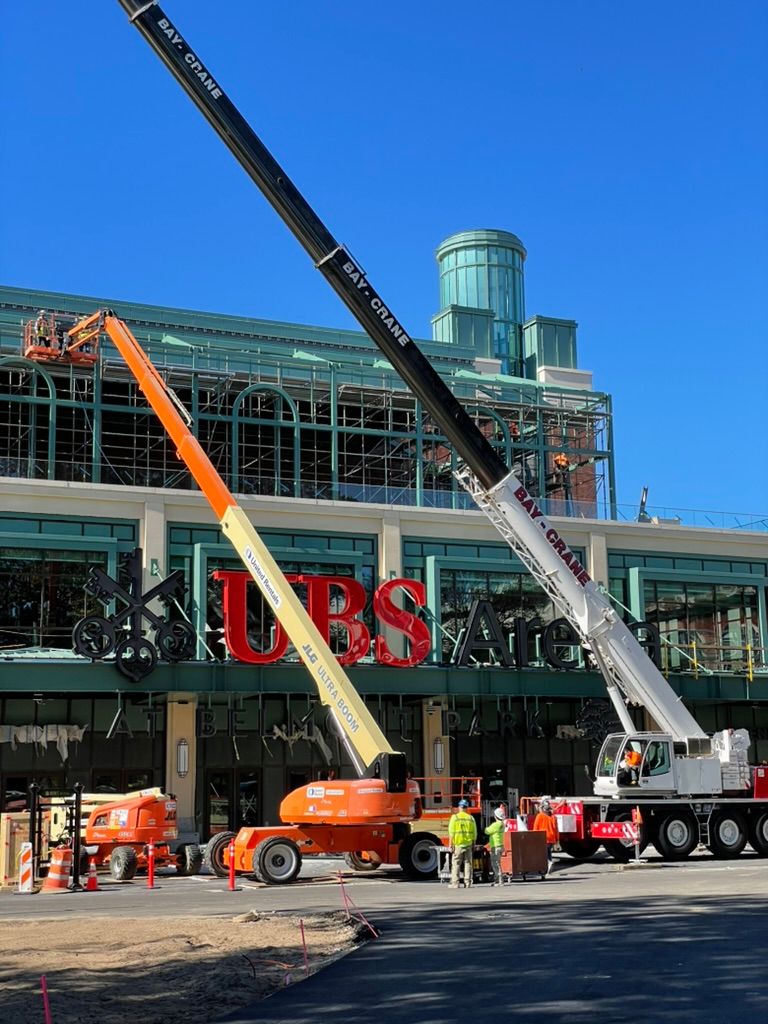 UBS Arena under construction at Belmont Park in Elmont, New York, showing installation of the arena’s exterior UBS signage ahead of opening. Love & War developed the conceptual design direction and guest experience strategy for UBS Arena, working with architects, interior designers and development teams to help shape the arena’s architecture, hospitality spaces, private clubs, food and beverage venues, suites, branded environments and connection to the larger Belmont Park redevelopment.