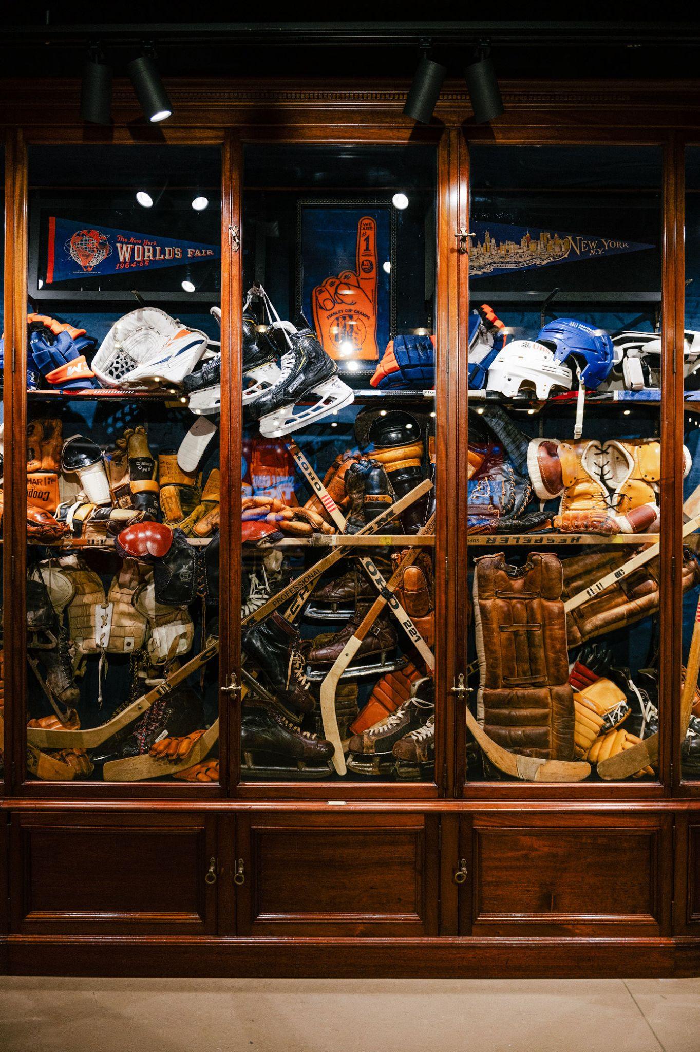 A curated display of vintage New York Islanders hockey equipment, including skates, helmets, gloves, sticks and goalie gear, inside Isles Lab at UBS Arena. Love & War developed the Isles Lab concept, naming, branding and retail experience, using Islanders history and hockey culture to create a distinctive alternative to the traditional NHL team store.