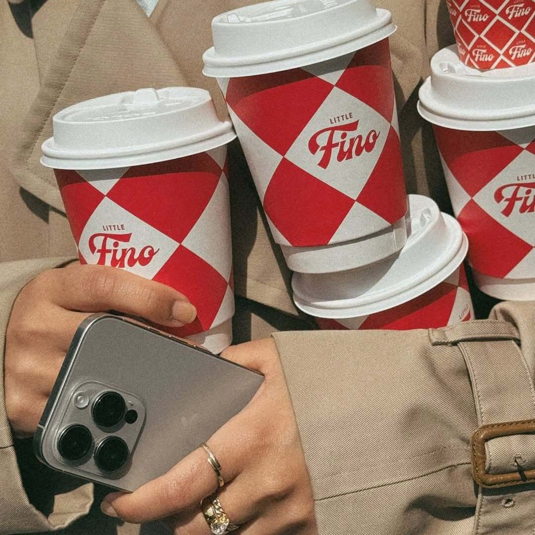 Custom red-and-white takeaway coffee cups for Little Fino, the all-day Italian café and bar at The William Vale in Williamsburg, Brooklyn, featuring a bold diamond pattern and Little Fino logo. Love & War developed the name, brand concept, visual identity and packaging for Little Fino, extending the Italian-inspired graphic system across coffee cups, menus, signage, uniforms, serveware and custom illustrations to create a recognizable hospitality brand rooted in classic Italian café culture and contemporary Brooklyn.