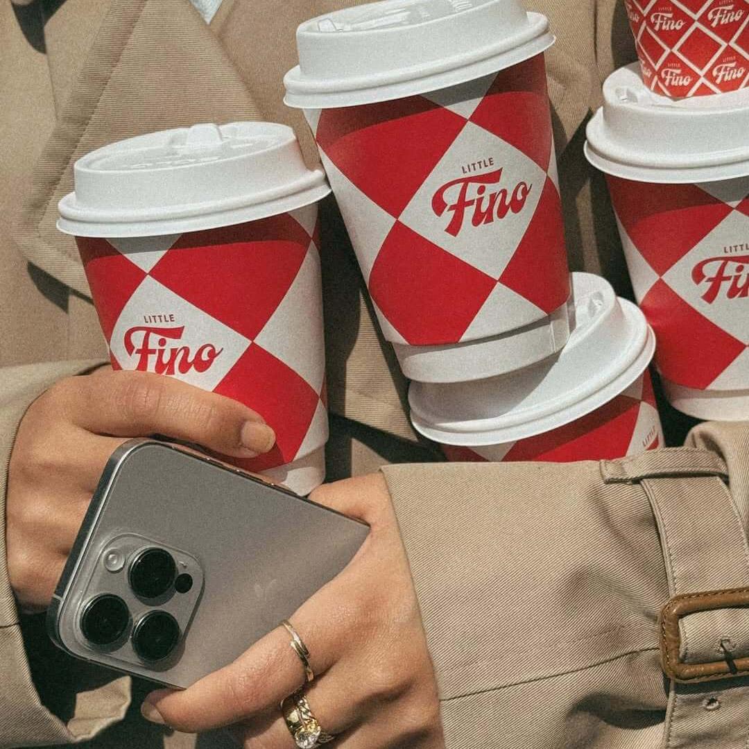 Custom red-and-white takeaway coffee cups for Little Fino, the all-day Italian café and bar at The William Vale in Williamsburg, Brooklyn, featuring a bold diamond pattern and Little Fino logo. Love & War developed the name, brand concept, visual identity and packaging for Little Fino, extending the Italian-inspired graphic system across coffee cups, menus, signage, uniforms, serveware and custom illustrations to create a recognizable hospitality brand rooted in classic Italian café culture and contemporary Brooklyn.
