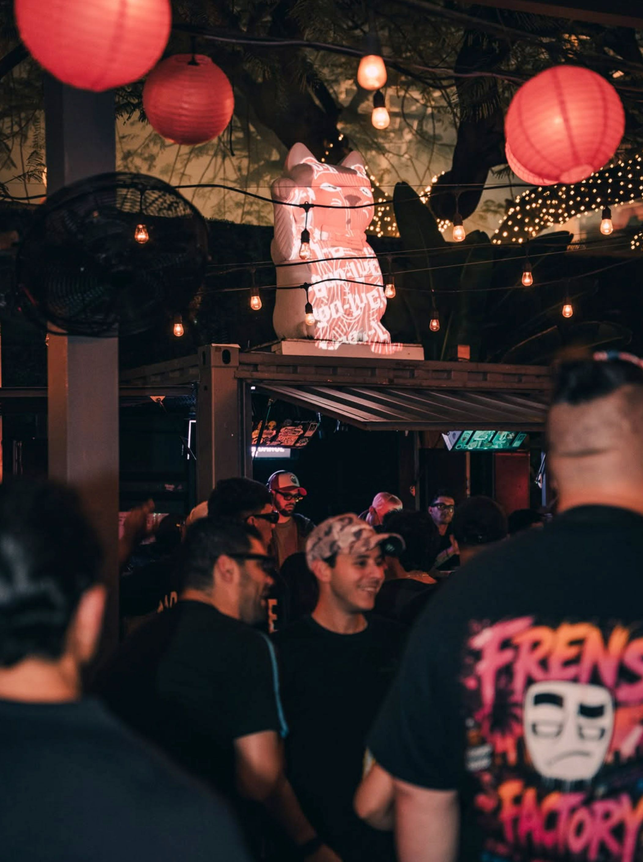 Nighttime scene at 1-800-Lucky with illuminated Lucky Cat signage, hanging lanterns and a DJ, capturing the venue’s nightlife atmosphere.